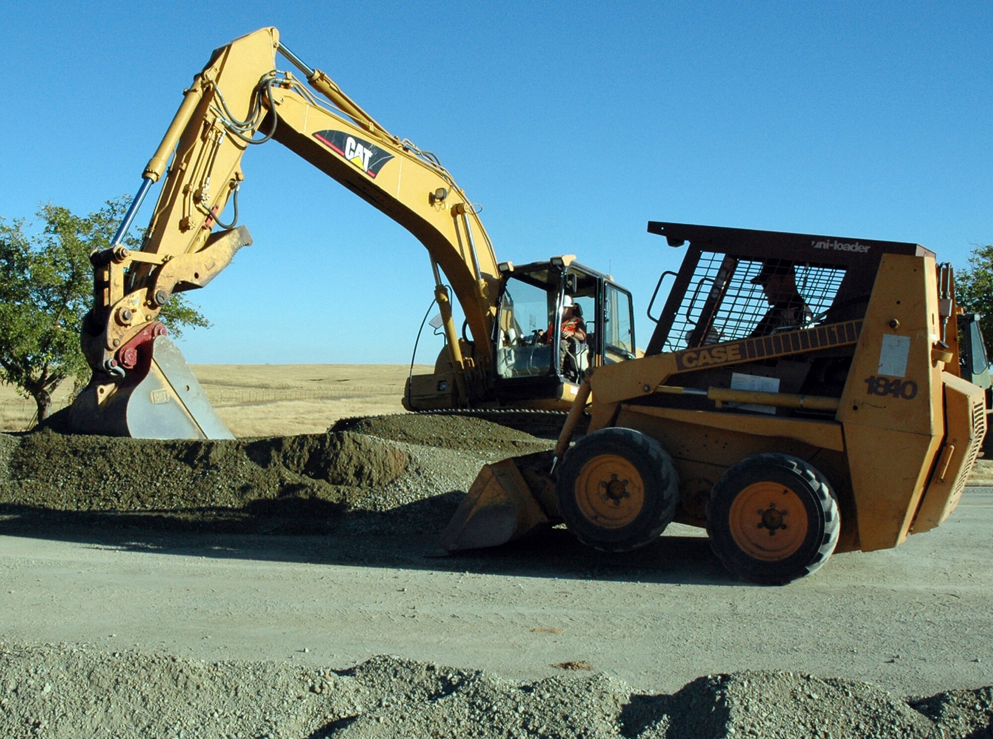 Technical Sgt. Al Fanini, utilities craftsman,uses a CAT excavator to dig as Master Sgt. Chris Estep, structural supervisor, moves gravel with a Bobcat. The two Reservists from the 940th Civil Engineer Squadron, Beale Air Force Base, Calif., worked with the active duty 9th CES team to complete road repairs on base Aug. 10-13, 2007.  Severe flooding more than two years ago caused culverts under the road bed to partially collapse and fill with rocks and debris. Team Beale civil engineers worked round the clock to complete the job. (US Air Force photo/Master Sgt. Ellen L Hatfield)
