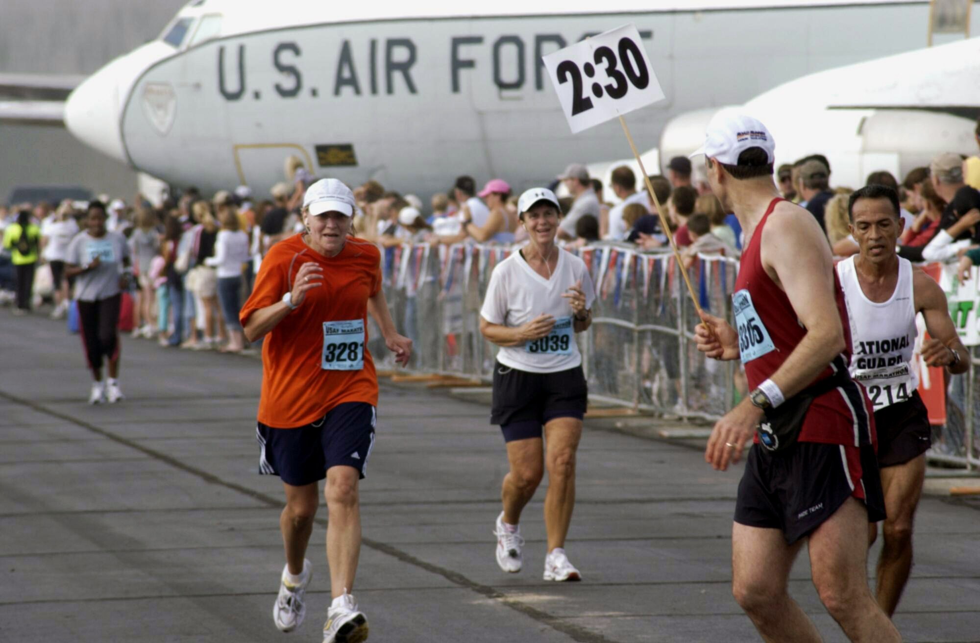 Participants in the 2006 Air Force Marathon come down the home stretch as Jim Crist (right), the lead pacer, looks on at Wright-Patterson Air Force Base, Ohio. (U.S. Air Force photo)

