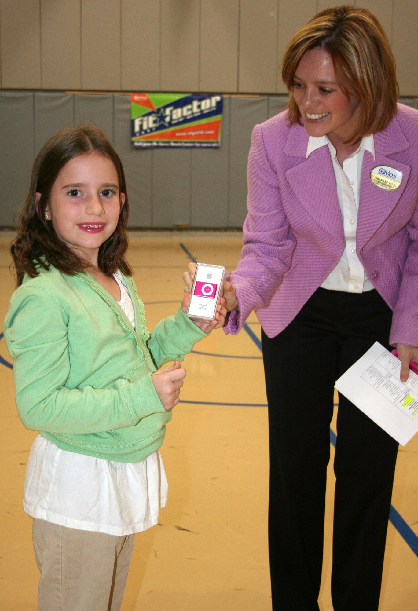 FAIRCHILD AIR FORCE BASE, Wash. – Stacy Compton, the youth support flight chief at the Youth Center, hands Mallory Moore an iPod Shuffle, the prize awarded to one FitFactor participant at each Air Mobility Command base. Mallory was noted as the winner for the month of July. Additional award winners will be announced in August and September, and a grand prize will be awarded Sept. 30 to mark the end of the program. (U.S. Air Force photo / Cara Burch) 