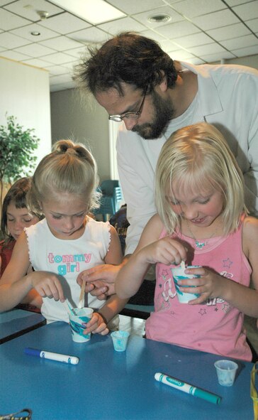 Brian Kinghorn adds glow-in-the-dark powder to seven-year-old Little Warrior Amber's  polymer slime. Little Warrior Morgan, 7, stirs the powder into her slime. The Science Adventures class taught students about the physical characteristics of polymers as well as lessons about electricity, electro-magnets, pneumatics, the principles of lift and flight, and the connection between the forces of balance and gravity. The class was held at the Malmstrom Youth Programs Center Aug. 13 to 17.  (U.S. Air Force photo/Airman 1st Class Dillon White).