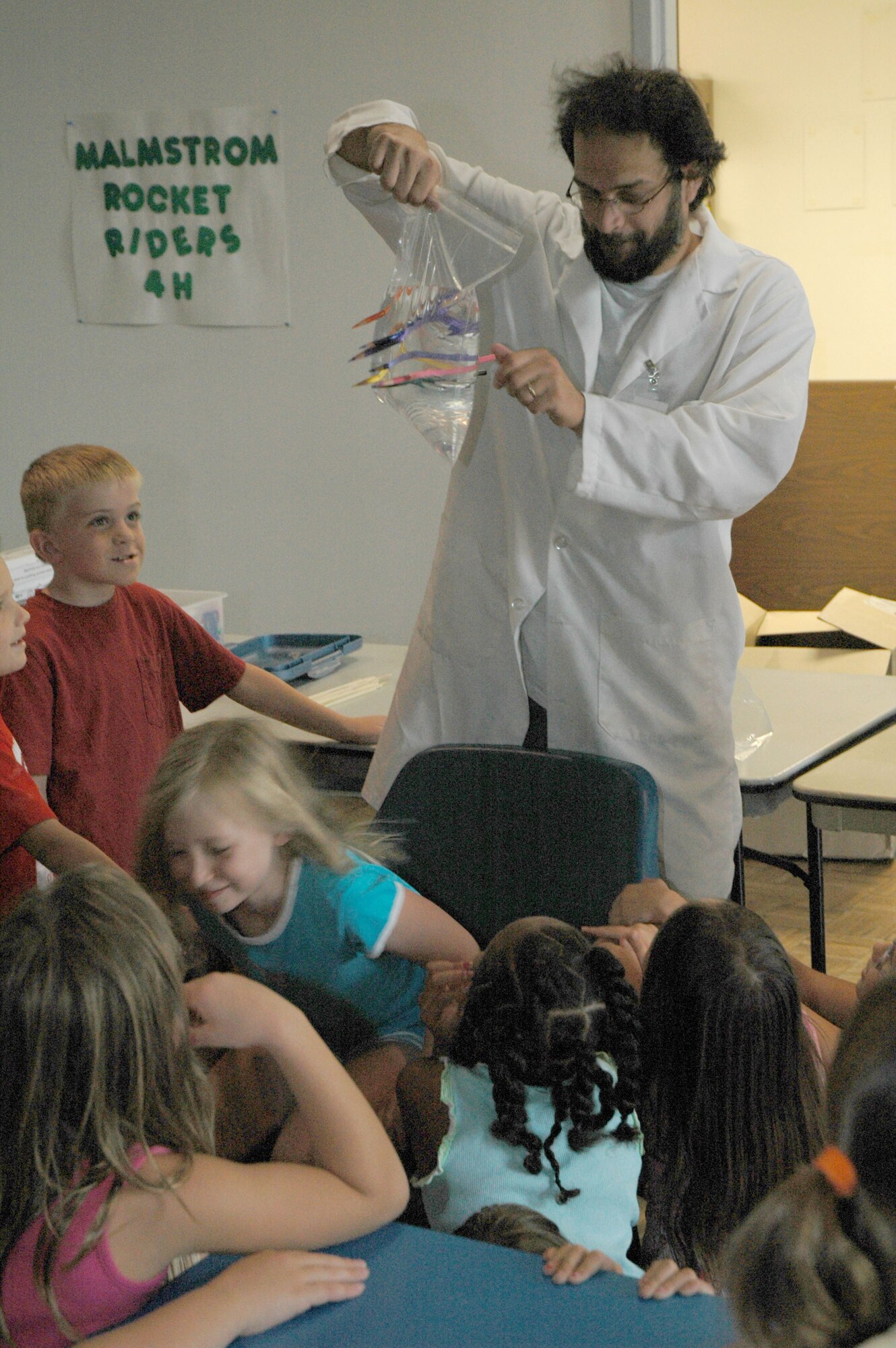 Brian Kinghorn holds a plastic bag pierced by pencils over Little Warrior Katie, 8 at the Malmstrom Youth Program Center "Gizmos, Gadgets and Goop" science fair Aug. 13 to 17. The class focused on the characteristics of polymers, chemcial reactions and inventions through the art of science. (U.S. Air Force photo/Airman 1st Class Dillon White).