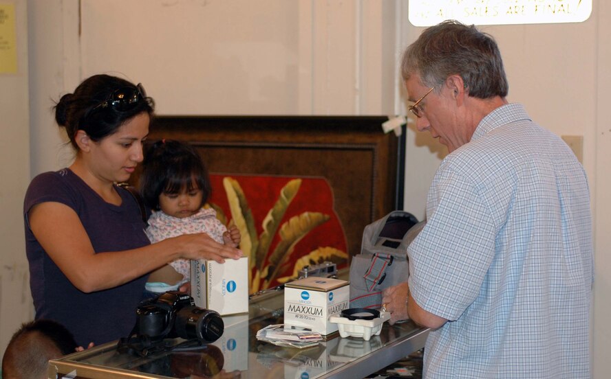 Mark McIntire, (right), Thrift Shop manager, helps customer Marta Pacada, with a camera purchase. Proceeds from the Thrift Shop are divided between the Officers and Enlisted Spouses clubs, which distribute that money for scholarships as well as other events, activities and organizations. (U.S. Air Force photo/ Nick DeCicco)