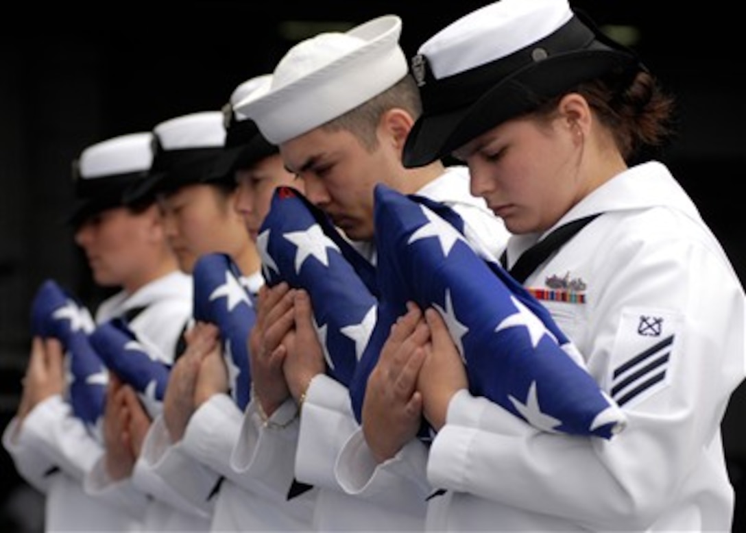 Sailors acting as flag bearers bow their heads during a prayer at a burial at sea ceremony aboard the aircraft carrier USS Abraham Lincoln (CVN 72) while under way in the Pacific Ocean on Aug. 19, 2007.  The Lincoln conducted the solemn and sacred tradition of burial at sea for 11 former service members during its transit to its homeport of Everett, Wash.  