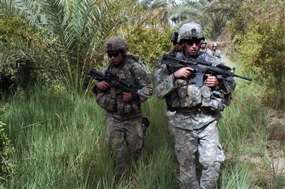 U.S. Army soldiers patrol through a palm grove.