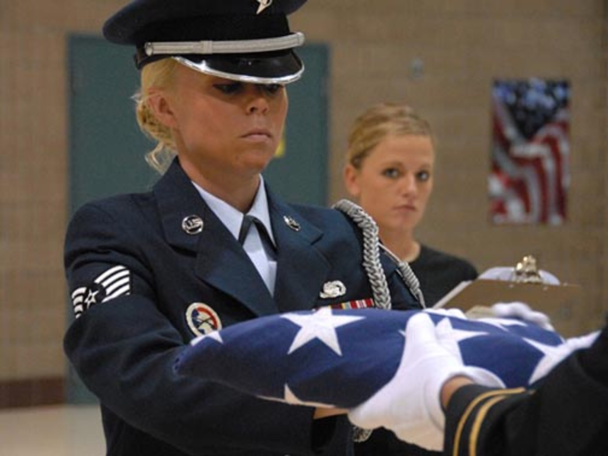 Technical Sgt. Jolene R. Savageau, 119th Wing, accepts the United States flag during a flag folding practice run on examination day as instructor PFC Kayla Staub, North Dakota Army National Guard, looks on with a critical eye.  (USAF photo/SMSgt. David Lipp)
