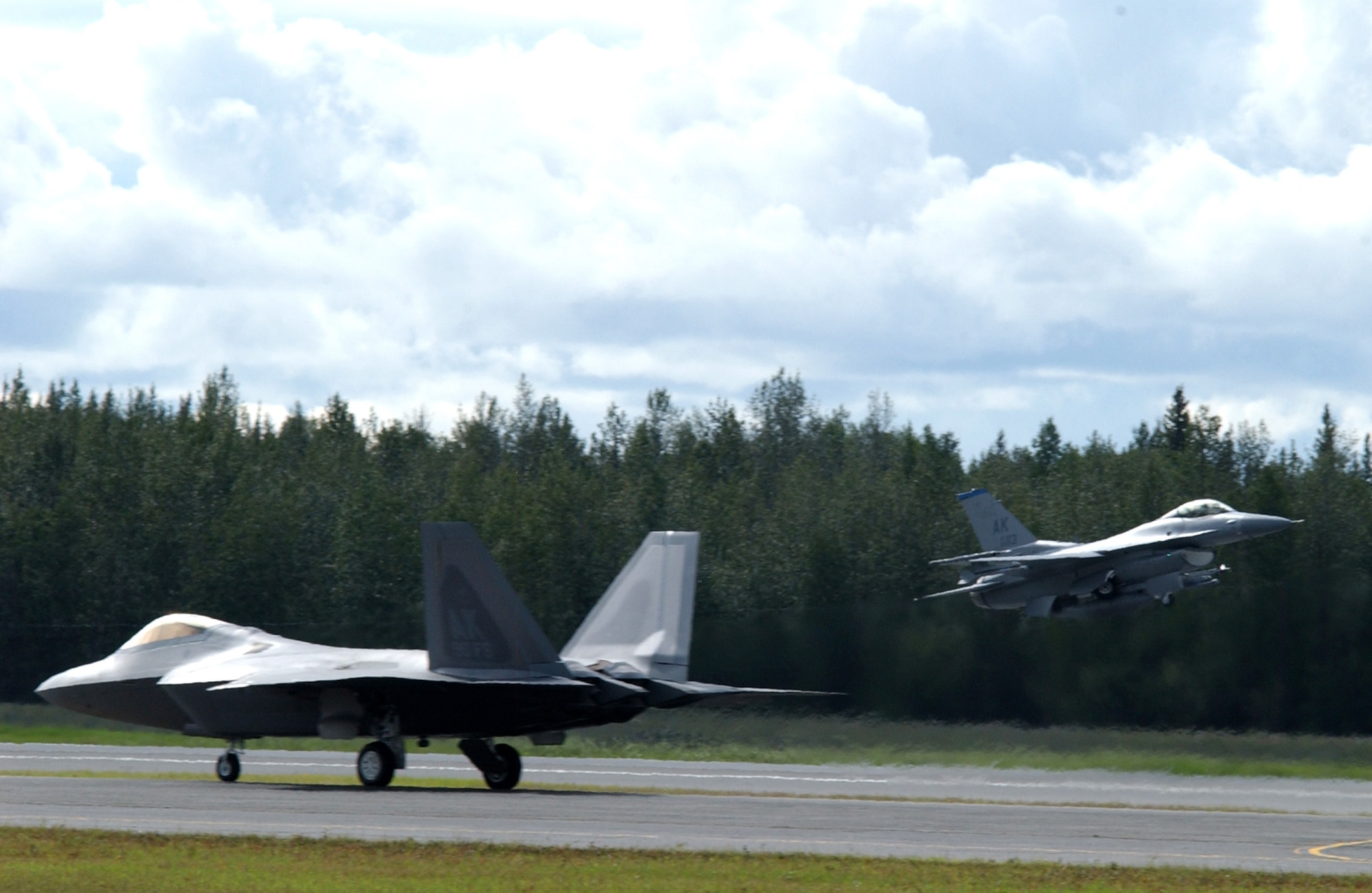 EIELSON AIR FORCE BASE, Alaska -- An F-22 Raptor taxi's down the Eielson AFB runway as an F-16 Falcon takes off Aug. 22, 2007. The F-22 was on static display during the 354th Fighter Wing change of command ceremony, and left soon after the ceremony was over.  (U.S. Air Force photo by Airman 1st Class Christopher Griffin)