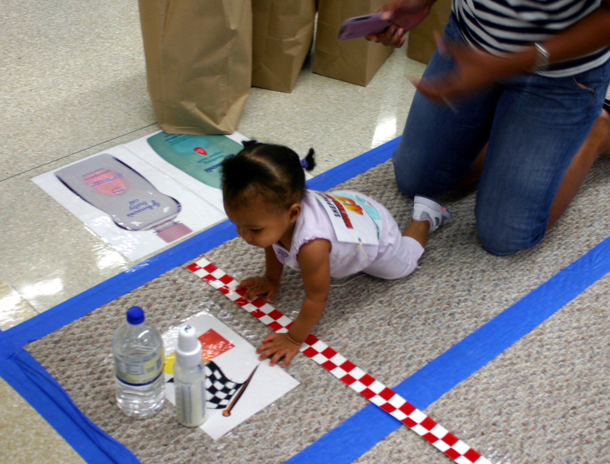Kaiden Wynne crawls over the finish line in pursuit of her bottle during the Hotter'N Heck diaper derby at the Commissary Aug. 26.  Wynne won second place in the 9-11 months category. (U.S. Air Force photo/Staff Sgt. Tonnette Thompson)
