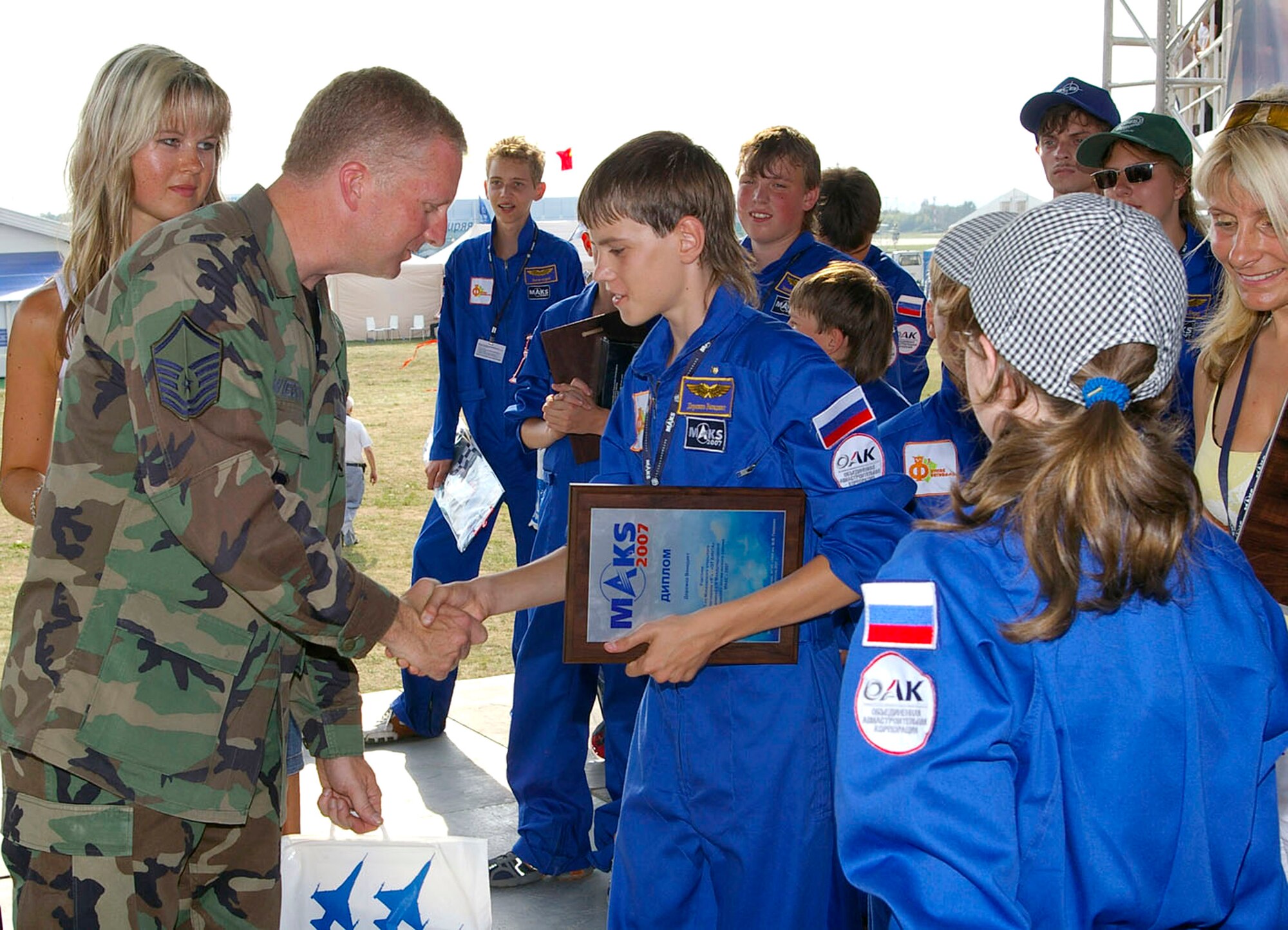 With the aid of a Russian interpreter, Master Sgt. Darrell Wiedenbeck presents gifts to Moscow children Aug. 23 at the Moscow International Air Show in Zhukovsky, Russia.  The children, ages 6 to 16, visited the show as part of a program called Moscow Open Festival for Children's Creativity. Approximately 60 children from nearby towns attended. Leading up to the festival, the children either made models or did artwork in four categories: Aviation, space craft, handcrafts and artwork. The top three winners in each group received prizes, and Airmen presented the children with additional aviation materials such as models of Air Force aircraft, pens, pencils and pins. The air show ran Aug. 21 to 26 and included Department of Defense participation of static displays and aerial flight demonstrations. Sergeant Wiedenbeck is assigned to Headquarters U.S. Air Forces in Europe at Ramstein Air Base, Germany. (U.S. Air Force photo/Karen Abeyasekere) 
