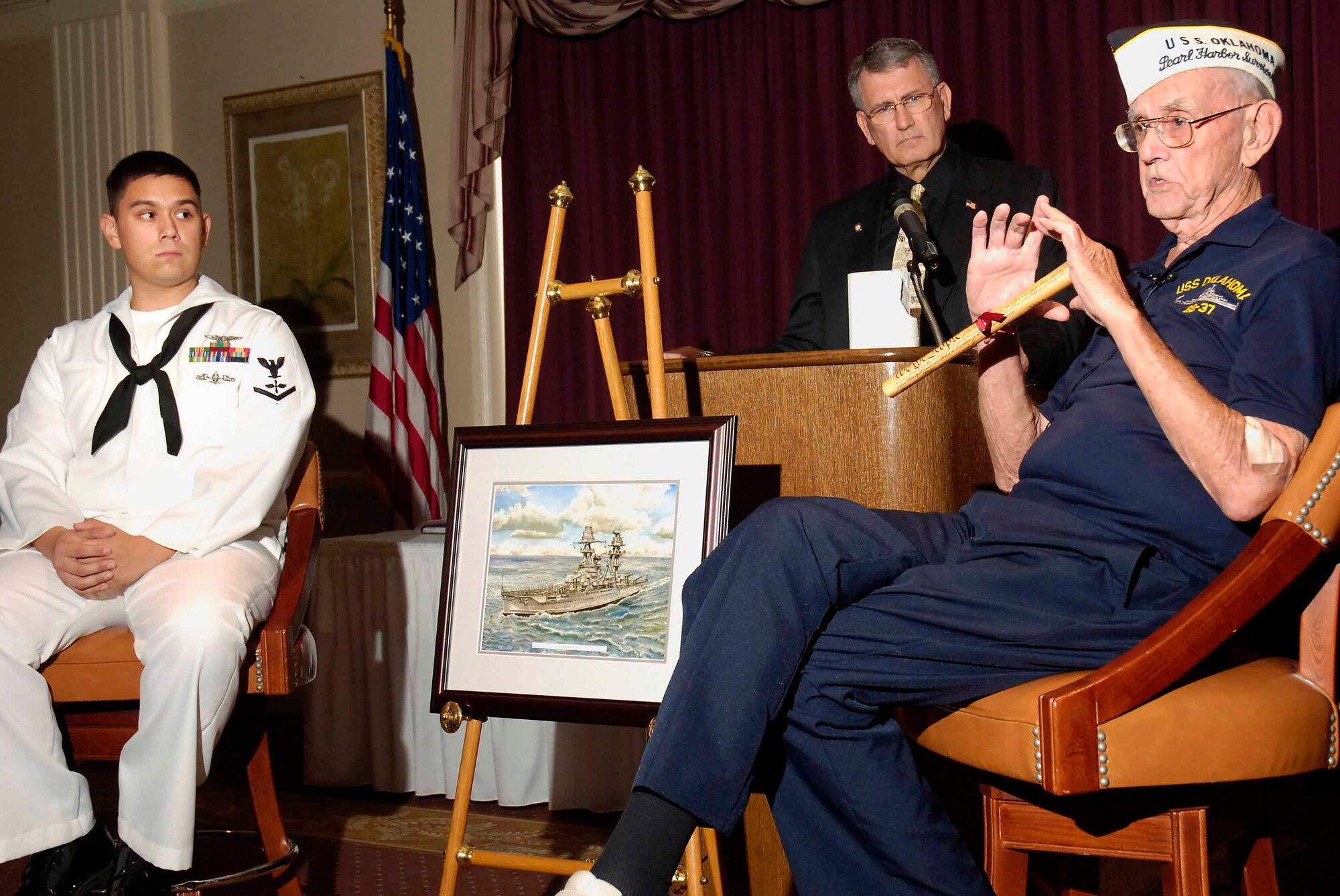 Petty Officer 3rd Class Kristofer Piros, Strategic Communications Wing ONE, and state Rep. Gary Banz listen during the Aug. 16 Tinker Management Association luncheon as USS Oklahoma survivor Paul Goodyear holds a copy of the U.S. Constitution he presented to Petty Officer Piros in a ceremony symbolizing passing the responsibility of defending the constitution from one generation to the next. (Air Force photo by Dave Faytinger)