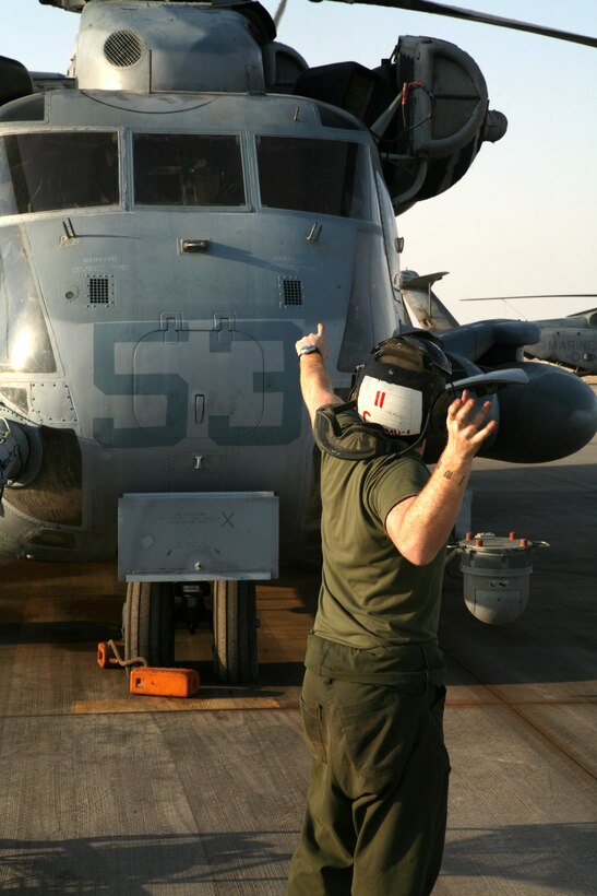 AL ASAD, Iraq - Lance Cpl. Taylor Conradi, an avionics technician with Marine Heavy Helicopter Squadron 466, uses hand signals to communicate with another Marine over the sound of the engines while performing maintenance on a CH-53E "Super Stallion," Aug. 29.