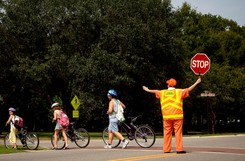 Faythe Deweese, Charleston AFB school crossing guard, helps Alyssa and Keeley Butters, daughters of Col. Anthony Butters, 437th Operations Group deputy commander, walk across Hill Boulevard with their mother, Kathleen, after school Wednesday on base.  (U.S. Air Force photo/Airman 1st Class Nicholas Pilch) 
