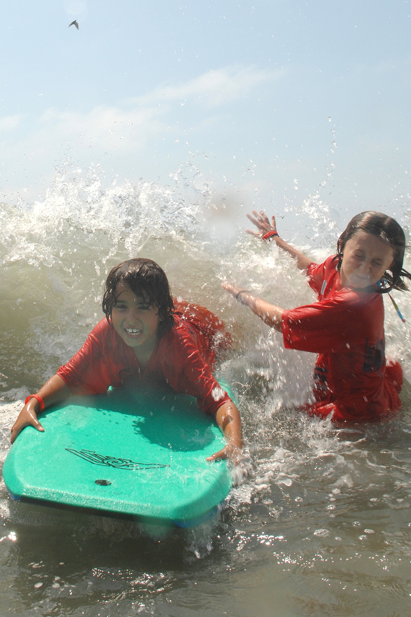 Robert McIntosh rides a wave on a boogie board while his friend, Katie, tries not to get splashed by the incoming wave during the Youth Summer Camp trip to Seal Beach, Aug 22. (Photo by Stephen Schester)