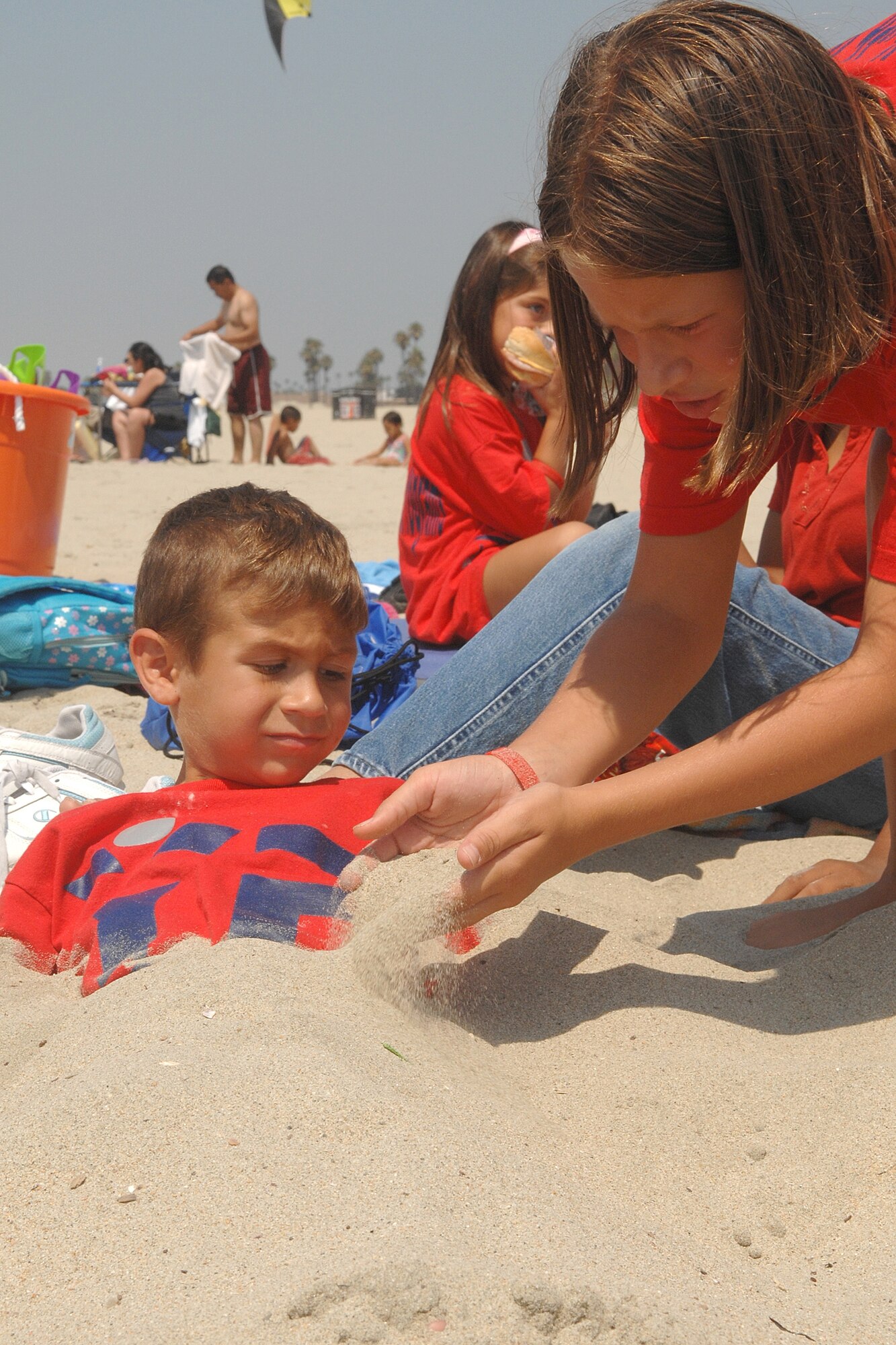 Sky Ochoa buries her brother, Zachery in the sand during the Youth Summer Camp trip to Seal Beach, Aug 22. (Photo by Stephen Schester)