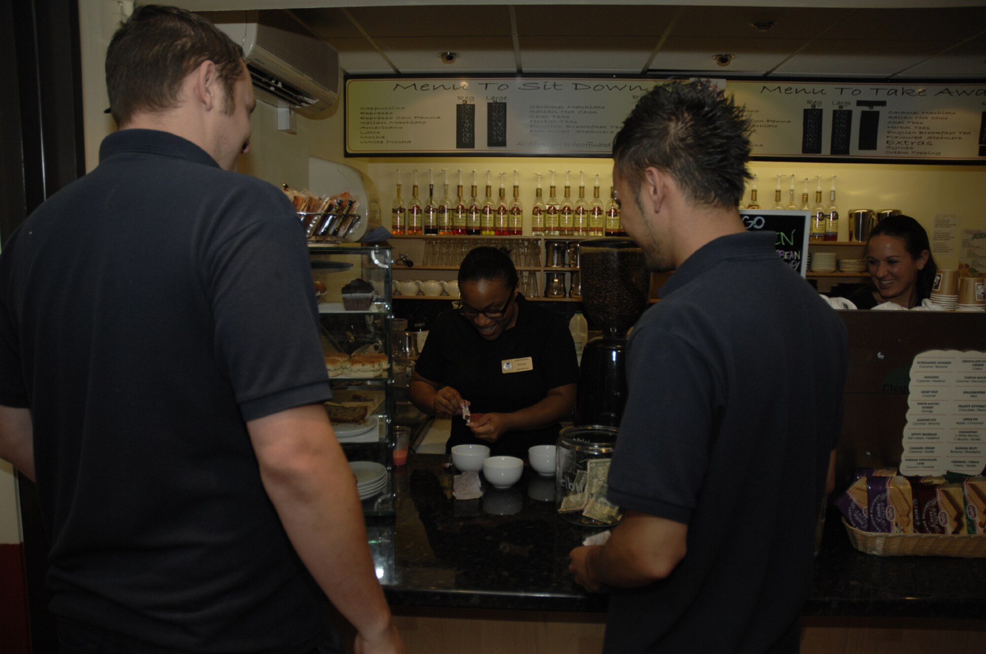 Tamia Bain prepares hot tea for two of RAF Lakenheath's civilian contractors Aug. 2 as coworker Stacey Disco looks on at the Jitterbean Café, 48th Fighter Wing Services Squadron. The café recently went green, offering patrons a discount for bringing in mugs instead of using disposable cups. (U.S. Air Force photo by Airman 1st Class Erika Brooke)