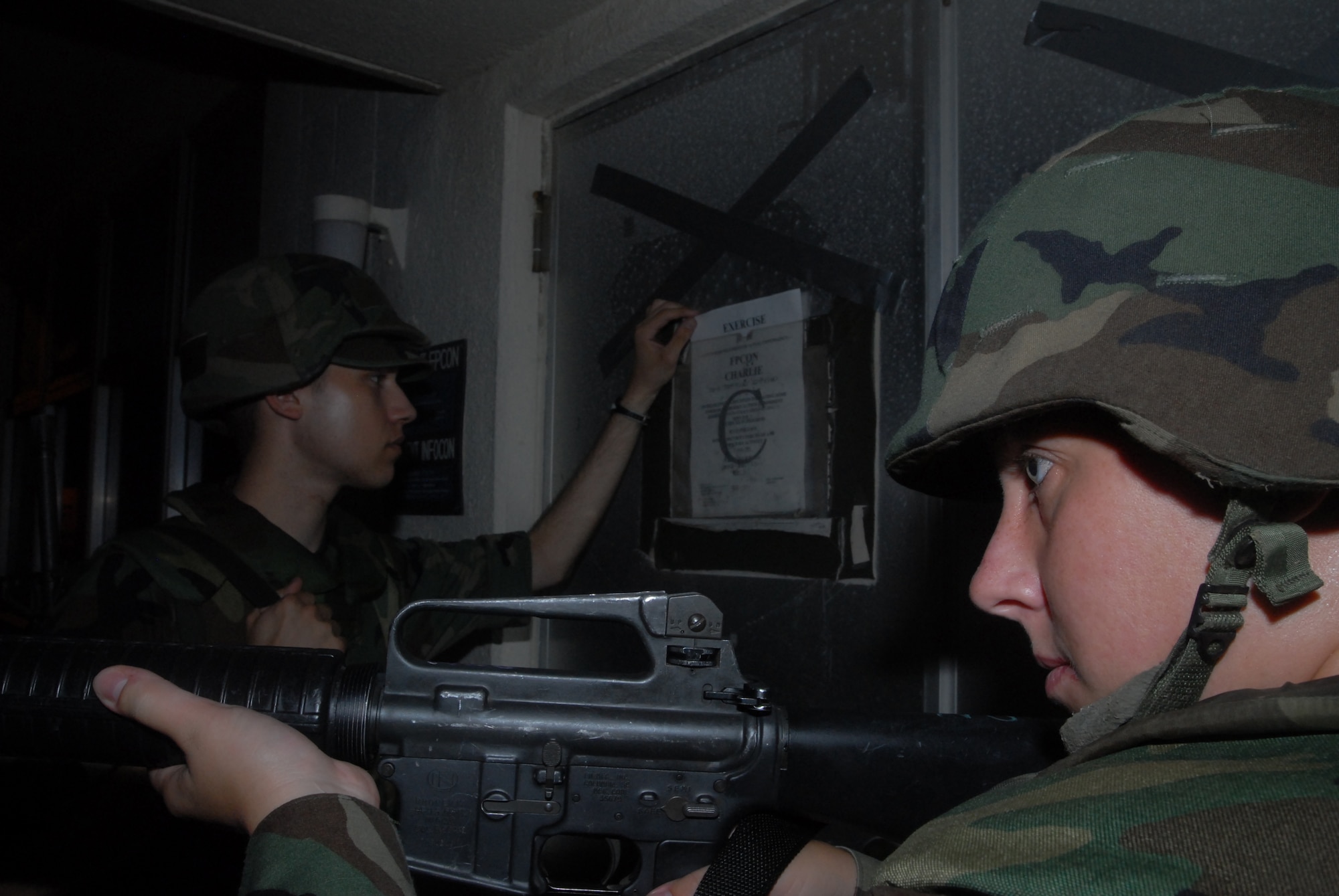 Airman 1st Class Tyler McCollom changes the Force Protection Signs while Senior Airman Mary Osterman provides security during a base exercise at Kadena Air Base, Japan, Aug. 23, 2007. Both Airmen took the selective arms course which enables them to protect their squadron's personnel and assets. The base conducted a three-day base exercise to demonstrate its ability to deploy and generate aircraft. Airman McCollom is a network application technician with the 18th Communications Sqaudron and Airman Osterman is an airfield systems technician with 18th Communications Squadron. (U.S. Air Force Photo/Senior Airman Darnell T. Cannady)