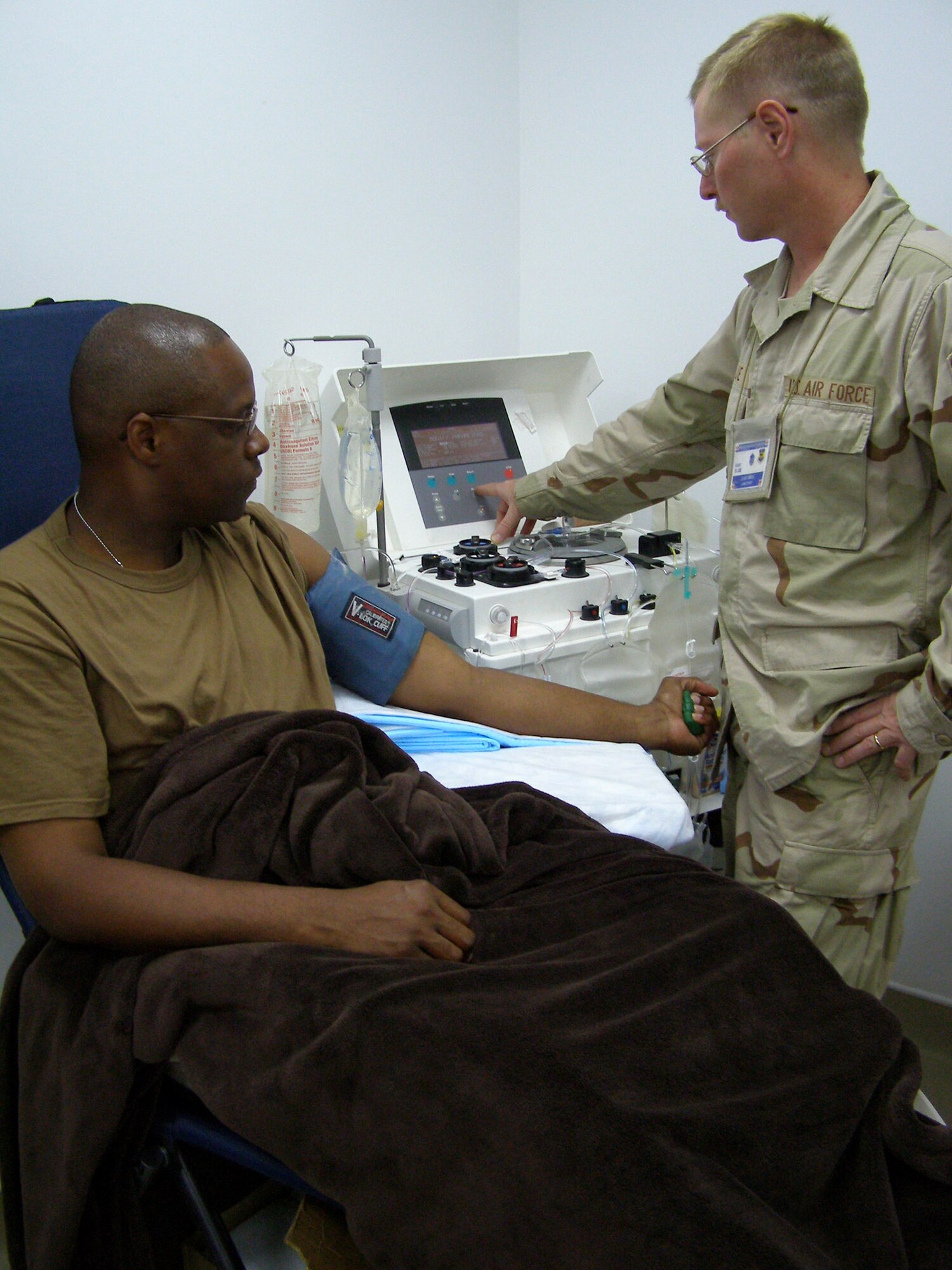 Master Sgt. Les Blue checks a haemonetics machine while Tech. Sgt. Darrin Sewer sits in the donor's chair Aug. 5 at Balad Air Base, Iraq. Sergeant Sewer donated the first plasma in the area of responsibility. Sergeant Sewer has type AB plasma, the universal plasma type. The plasma will be used to supplement current supplies that are sent from the states. Sergeant Blue is a lab technician and NCO in charge of the Air Force Theater Hospital Apheresis Center. Sergeant Sewer is the NCO in charge of the 332nd Expeditionary Communications Squadron help desk. (U.S. Air Force photo/Staff Sgt. Michael Garcia)