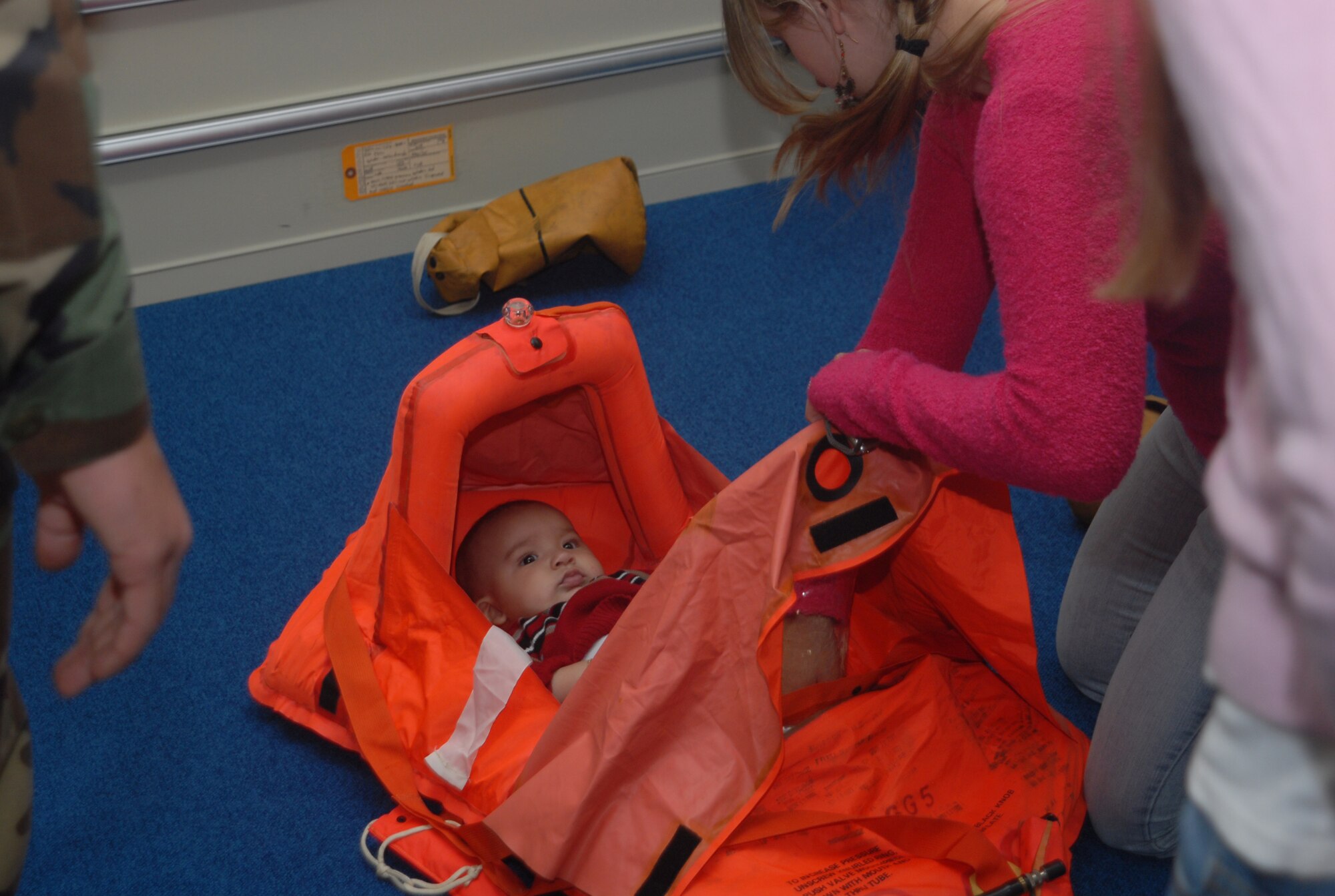 A mother places an infant in a small life raft designed specifically for babies as part of a tour through the 18th Operations Support Squadron Nov. 30, 2007. The squadron opened its doors to the spouses as a way of thanking them for their support.  (U.S. Air Force photo/Staff Sgt. Christopher A. Marasky)