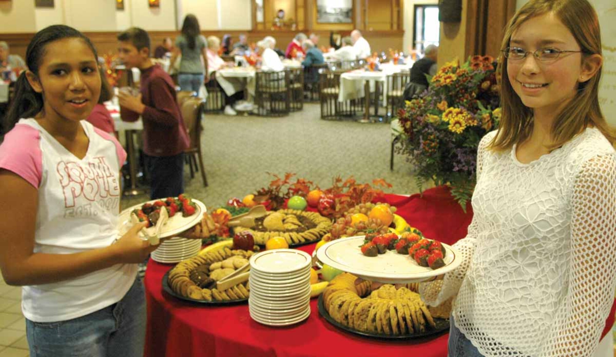 Mia Lusty, 11, and Rachel Wilsey, 13, make a quick stop at the dessert table to load up on chocolate covered strawberries and cookies to handout to guests during dinner.  Mia is the daughter of Master Sgt. Andre Lancaster and Rachel’s father is First Sergeant Master Sgt. Michael Wilsey.  (Air Force photo by Kathy Paine)

