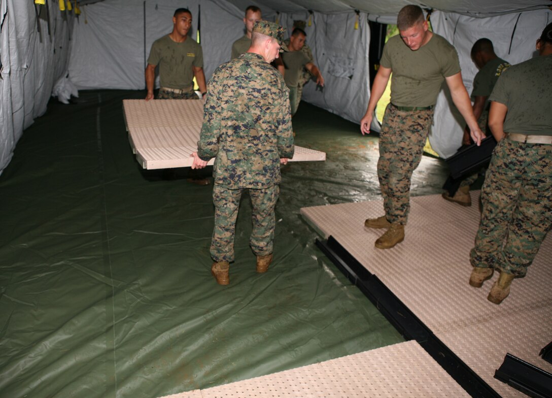 Gunnery Sgt. Michael D. Molina, supply chief, HQSVCBN, MARFORPAC, directs traffic while his Marines install the flooring to the Command Operation Center that was built during exercise Thunderdome 2007, Dec. 5.