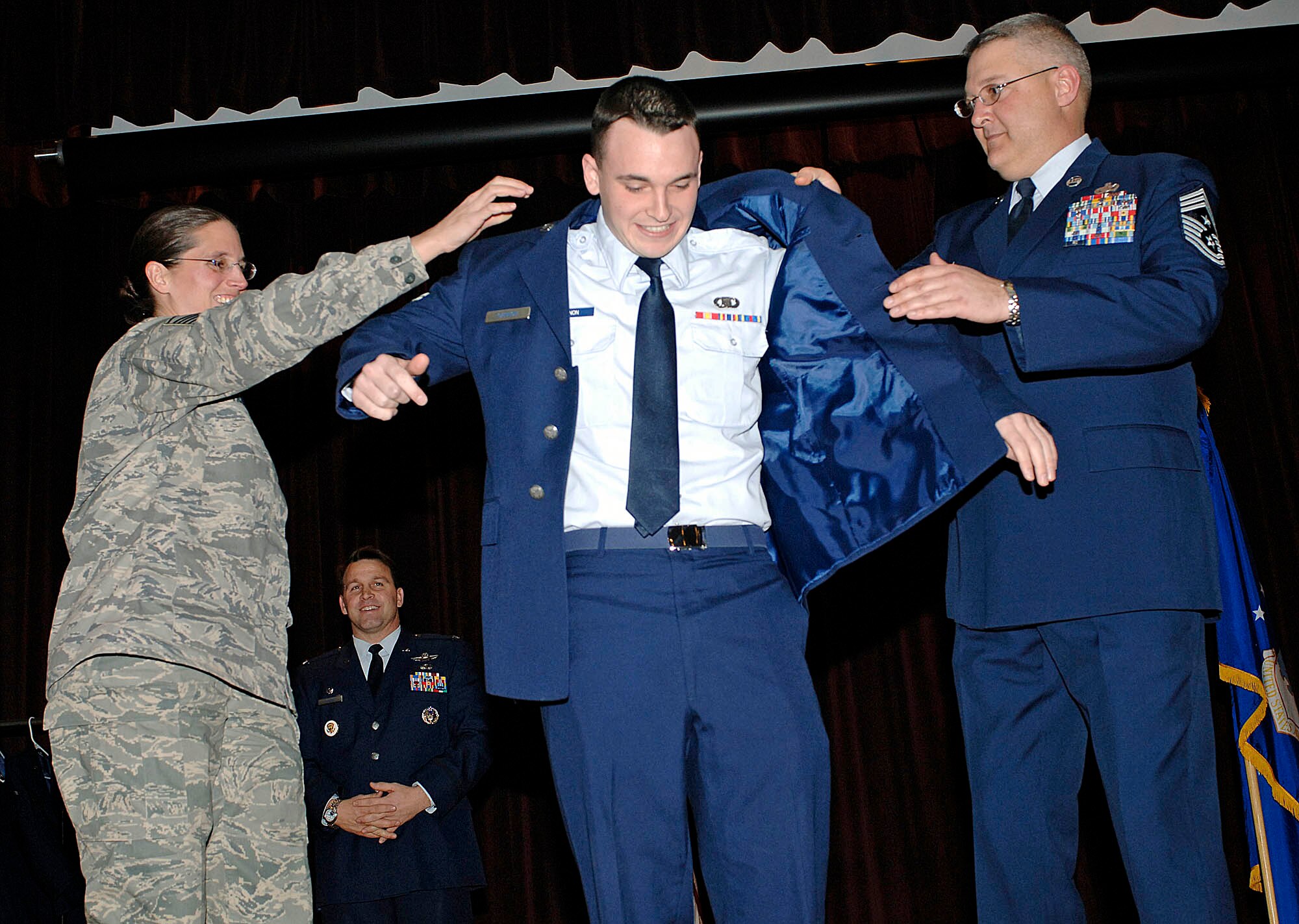 FAIRCHILD AIR FORCE BASE, Wash. – Master Sgt. Nancy Huber, 92nd Air Refueling Wing command post superintendent, and Command Chief Master Sgt. Paul Sikora, 92nd Air Refueling Wing, assist Airman Brandon Gannon, 92nd Air Refueling Wing command post junior controller, with trying on his service coat and newly acquired airman-first-class stripes during the promotion ceremony Nov. 30, as Col. Thomas Sharpy, 92nd Air Refueling Wing commander, looks on. (U.S. Air Force photo / Staff Sgt. JT May III)