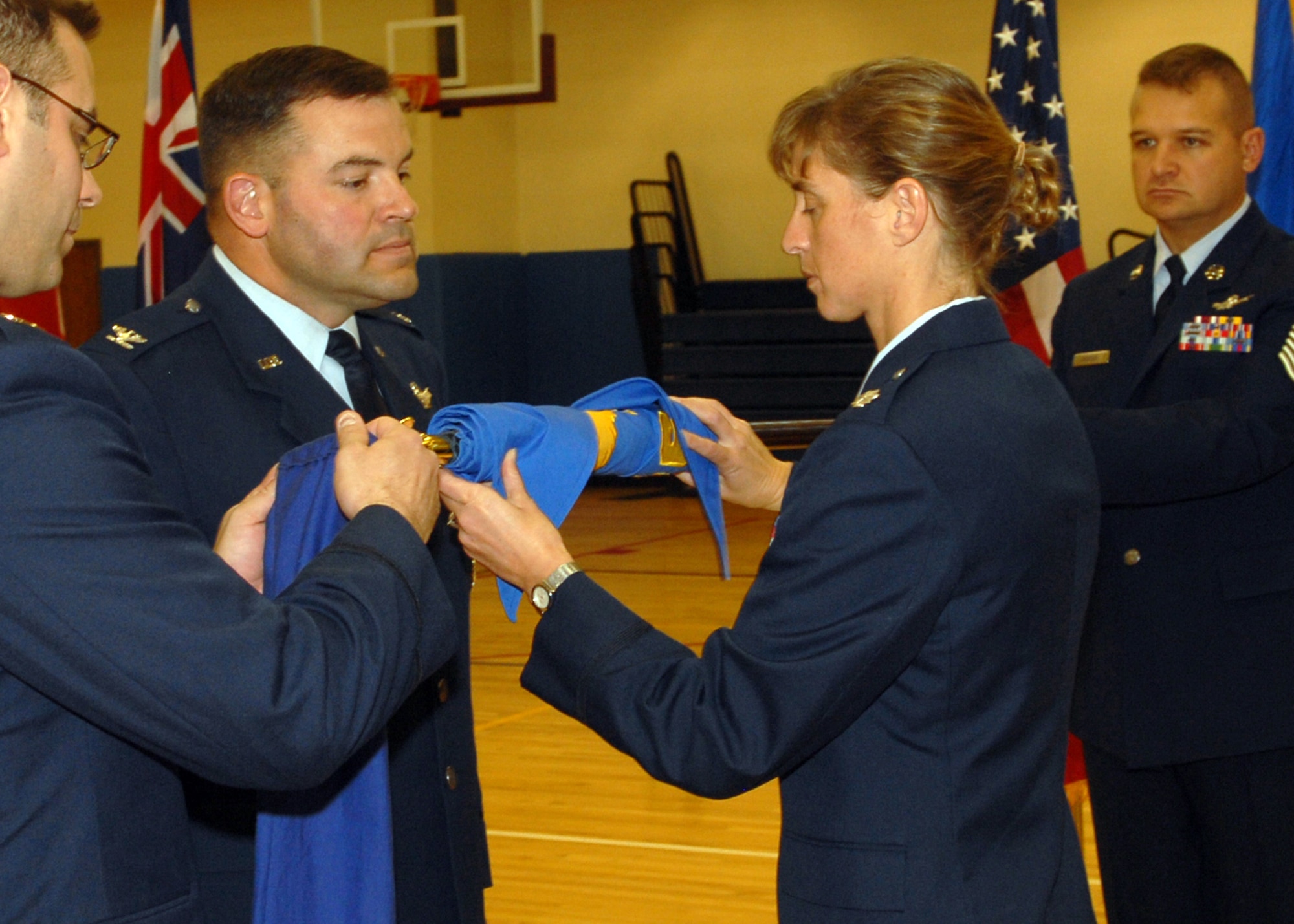 BUCKLEY AIR FORCE BASE, Colo. -- Lt. Col. Holly Weik, 11th Space Warning Squadron commander, and Col. Christopher Ayres, 460th Operations Group commander, furl the guidon of the 460th Operations Group, Detachment 1, to symbolize the de-activaion of the detachment. On Dec. 3, the 460th OG, Det. 1, stood down as the 11th SWS stood up in a ceremony held at the Buckley Fitness Center. (U.S. Air Force photo by Airman 1st Class Alex Gochnour)