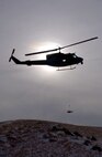 The silhouette of a UH-1N Huey helicopter from the 40th Helicopter Squadron hovers over the Montana skyline near the Rocky Mountain Front during a search and rescue training sortie Nov. 19. The stokes litter, a stretcher designed to transport people from the ground to the helicopter while in the air, is slowly lowered by the on-board flight engineer for a simulated search and recovery mission. (U.S. Air Force photo/Senior Airman Eydie Sakura).            