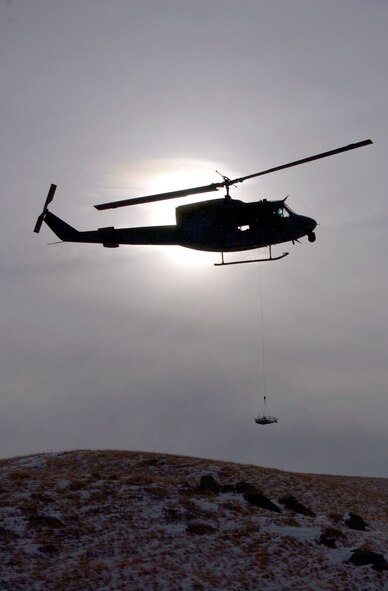 The silhouette of a UH-1N Huey helicopter from the 40th Helicopter Squadron hovers over the Montana skyline near the Rocky Mountain Front during a search and rescue training sortie Nov. 19. The stokes litter, a stretcher designed to transport people from the ground to the helicopter while in the air, is slowly lowered by the on-board flight engineer for a simulated search and recovery mission. (U.S. Air Force photo/Senior Airman Eydie Sakura).            