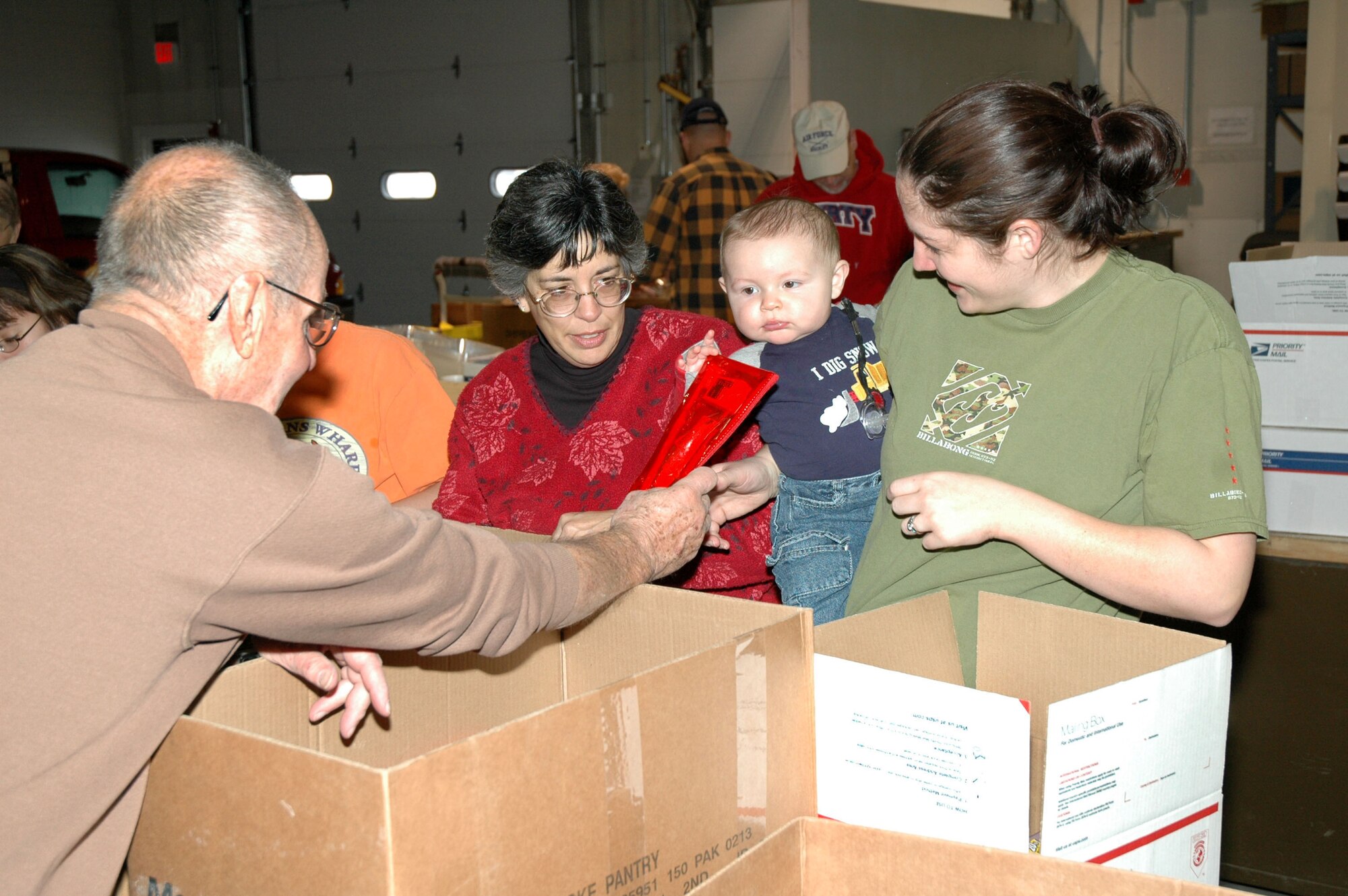Little Warrior Axel, 8 months, reaches for a dental hygiene kit from Al Maflin to add to a care package as Karen Helms and Jaine Springer watch. Roughly 400 care packages were shipped the same day to deployed servicemembers from Montana. (U.S. Air Force photo/Airman 1st Class Dillon White)