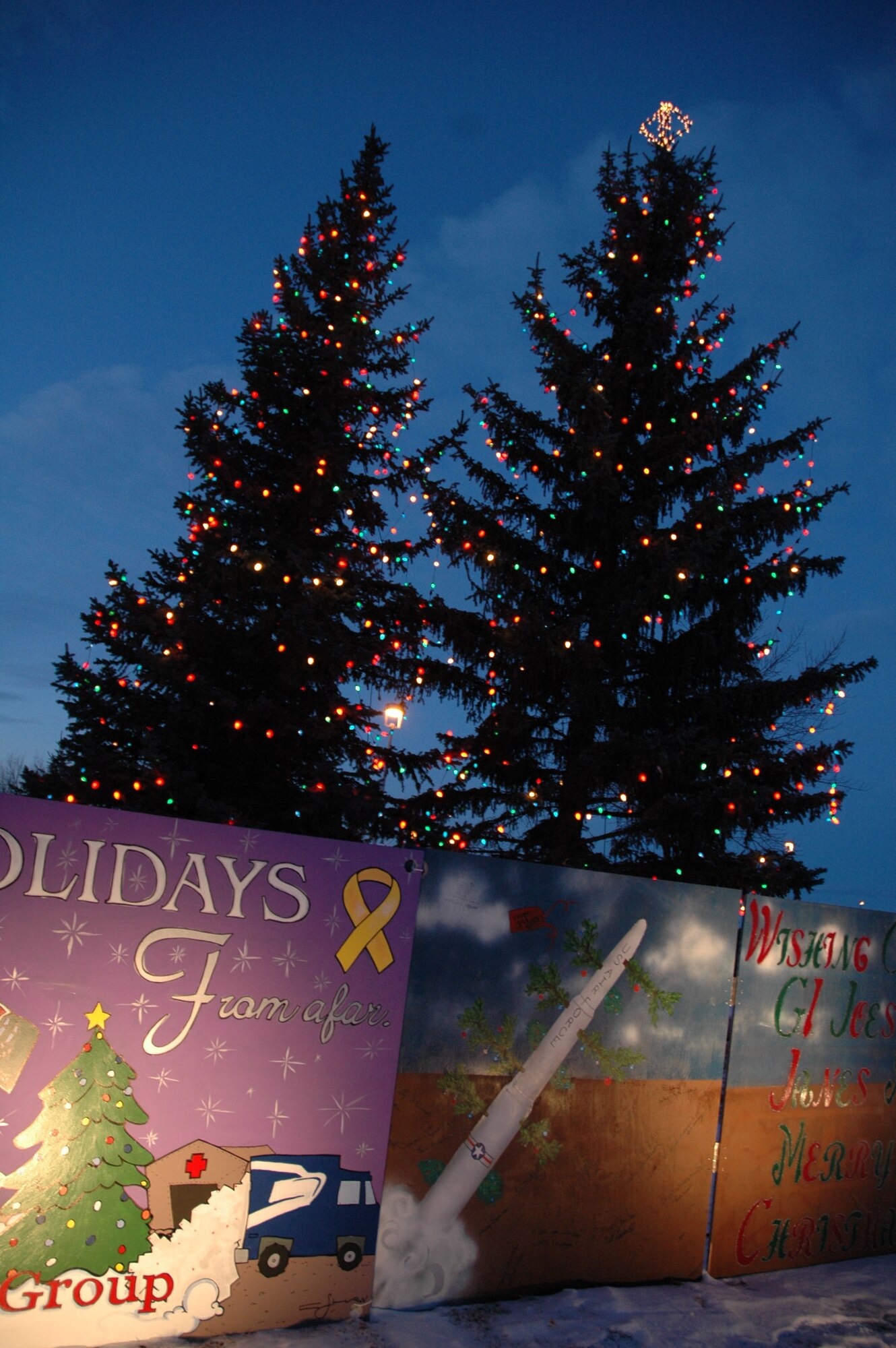 About 50 Airmen and their families watched trees outside the Grizzly Bend Club shine during the annual tree lighting ceremony Nov 29. Entries from the annual holiday-card contest rest under their bows. The 341st Medical Operations Group took first place in the card contest; the 341st Mission Support Squadron took second; and the 341st Comptroller Squadron took third. The 4-foot-by-8-foot decorated cards will remain on display in front of the Grizzly Bend Club this holiday season. (U.S. Air Force photo/Airman 1st Class Dillon White)