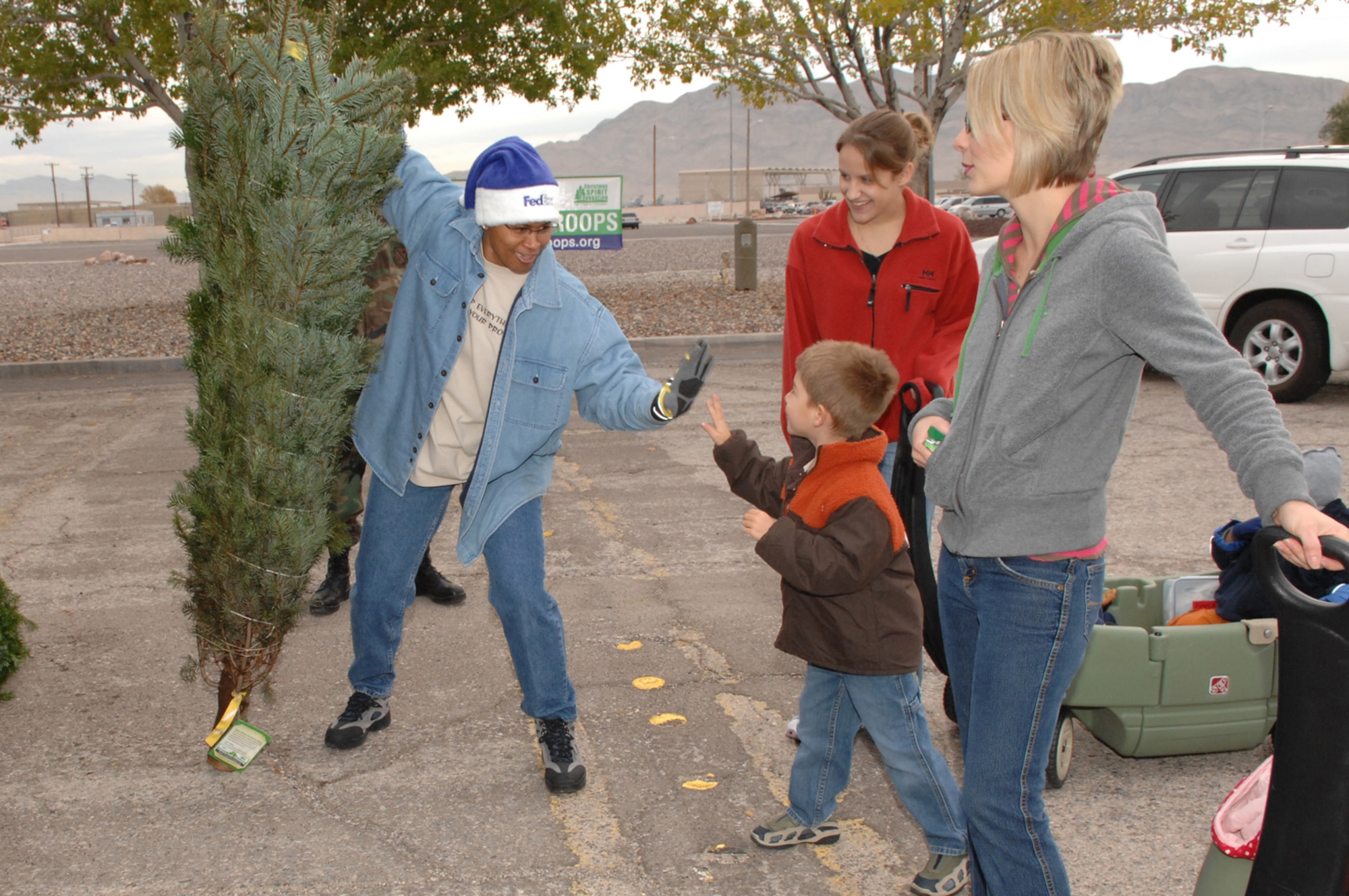 Master Sgt. Ileather Maxwell, 99th Medical Group superintendent of laboratory services (left), celebrates with the Wallace family after they picked out their first Christmas tree at the Trees for Troops event held Dec. 5 at Nellis AFB. To help spread holiday cheer, The Christmas Tree Foundation and FedEx donated 700 trees to Nellis Airmen free of charge. (U.S. Air Force photo by Airman 1st Class Kasabyan D. McGarvey)