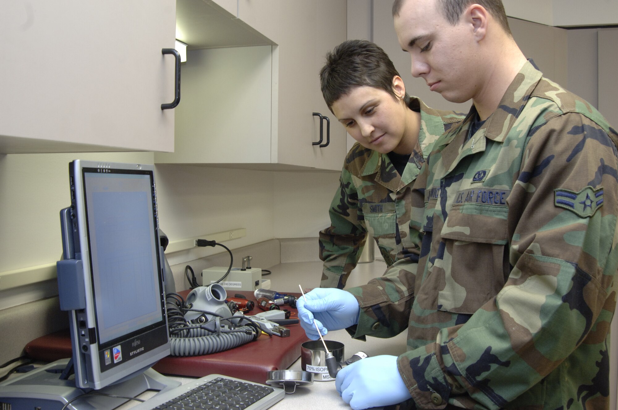 MCCONNELL AIR FORCE BASE, Kan. -- 22nd Operations Support Squadron, Aircrew Flight Equipment technicians, Airman 1st Class Christina Smith watches Airman 1st Class Cody Jaglowicz clean an oxygen regulator connector.  Every 90 days the Aircrew Flight Equipment technicians have to inspect and clean all helmets.  The Aircrew Flight Equipment provides and maintains the survival equipment for the air crew personnel.  (Photo by Tech. Sgt. Chyrece Campbell)