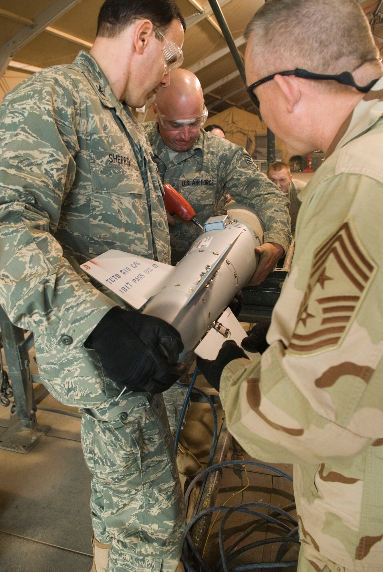 BALAD AIR BASE, Iraq -- Col. Steven Shepro, 332nd Air Expeditionary Wing vice commander, and Chief Master Sgt. Paul Wheeler, 332nd AEW command chief, hold up a fin kit as Staff Sgt. Gary Lawrence, 332nd Expeditionary Maintenance Squadron Ammunitions Flight, attaches it to the bomb body here, Dec. 5. Sergeant Lawrence who is deployed from Buckley Air Force Base, Colo. was able to work alongside wing leaders during the bomb build. Colonel Shepro is deployed from Pope Air Force Base, N.C., Chief Wheeler is deployed from Dyess Air Force Base, Texas. (U.S. Air Force photo/Staff Sgt. Joshua Garcia)