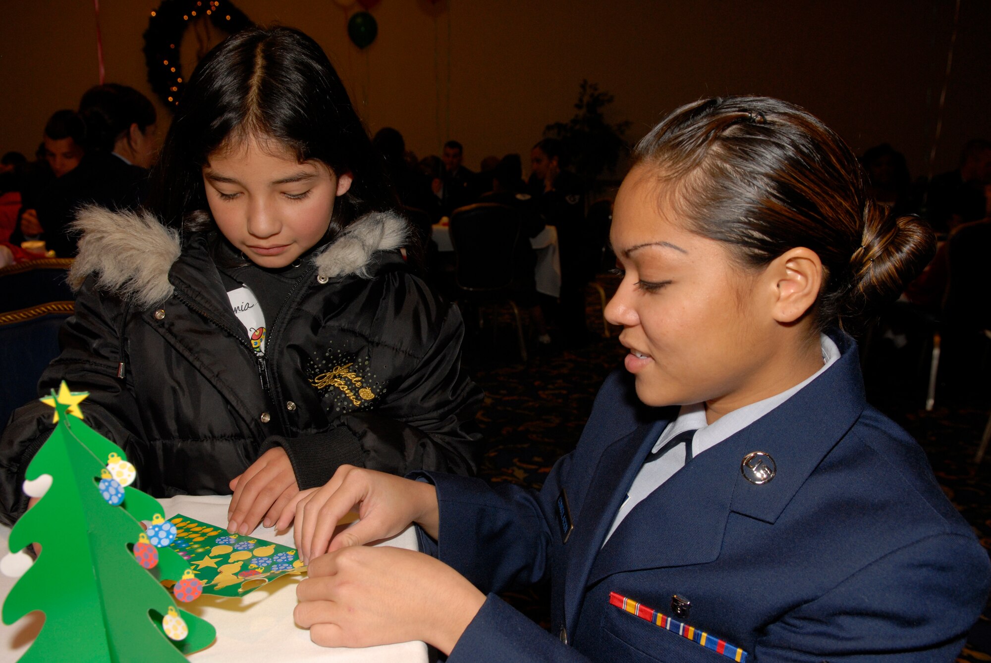 VANDENBERG AIR FORCE BASE, Calif.-- Stephanie Moreno, 11, and Airman 1st Class Lady Renee Consolacion, 30th Medical Group, craft a paper Christmas Tree during Operation Kids Christmas on Dec. 1.  Operation Kids Christmas is an annual event which involves about 200 children. Each child is assigned to an Airman and spends the day watching a magic show, making crafts, hearing an opera singer, and of course meeting Santa. (U.S. Air Force photo\Airman 1st Class Adam Guy)   