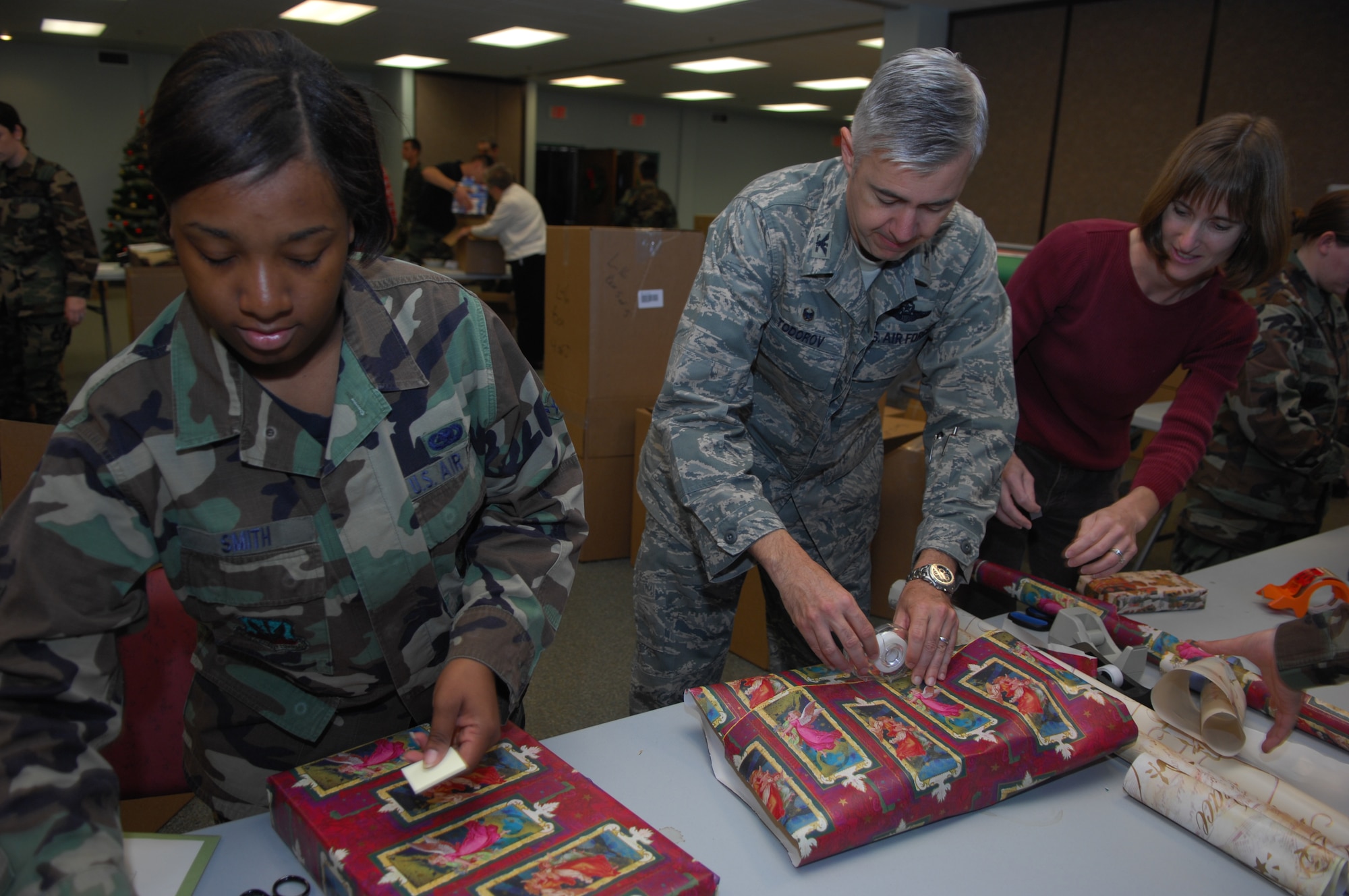 MOODY AIR FORCE BASE, Ga. — Airman Marquita Smith, 23rd Logistic Readiness Squadron training technician, and Col. Kenneth Todorov 23rd Wing Commander, wrap gifts Dec 6.  Team Moody participates in the Adopt-A-Family program to give back to the local community. (U.S. Air Force photo by Senior Airman Angelita Lawrence)