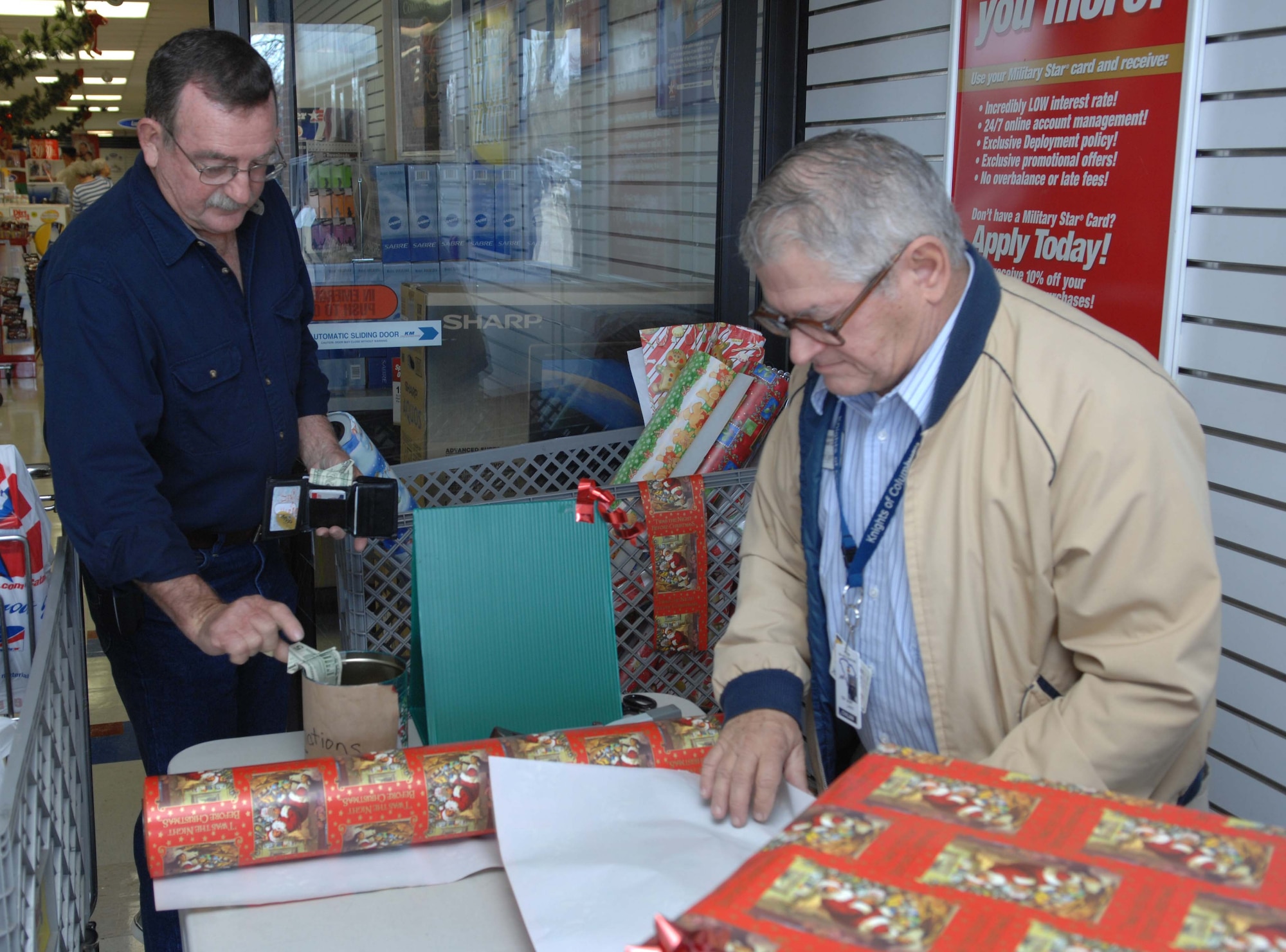 SHAW AIR FORCE BASE, S.C. -- Lonnie Truesdale makes a donation while Larry Huff, acting station chairman for the Red Cross, wraps a gift at the Base Exchange Dec. 11. Volunteers are wrapping gifts for donations at the BX until Dec. 22 to raise money for the American Red Cross. (U.S. Air Force photo/Airman 1st Class William Coleman)