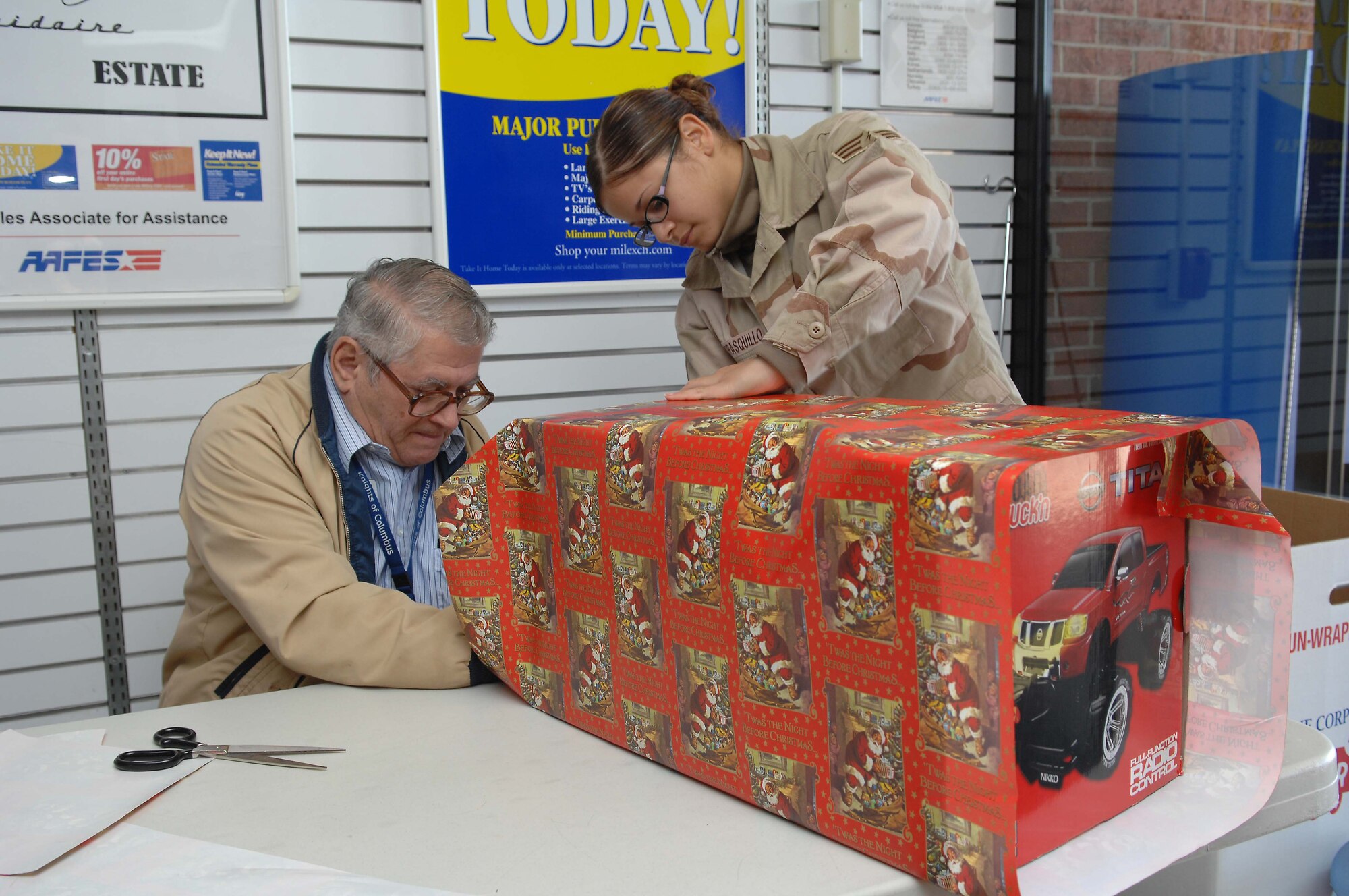 SHAW AIR FORCE BASE, S.C. -- Larry Huff, acting station chairman for the American Red Cross, and Senior Airman Cassie Carrasquillo, 609th Air Intelligence Squadron, wrap a gift at the Base Exchange Dec. 11. Volunteers are wrapping gifts for donations at the BX until Dec. 22 to raise money for the Red Cross. (U.S. Air Force photo/Airman 1st Class William Coleman)