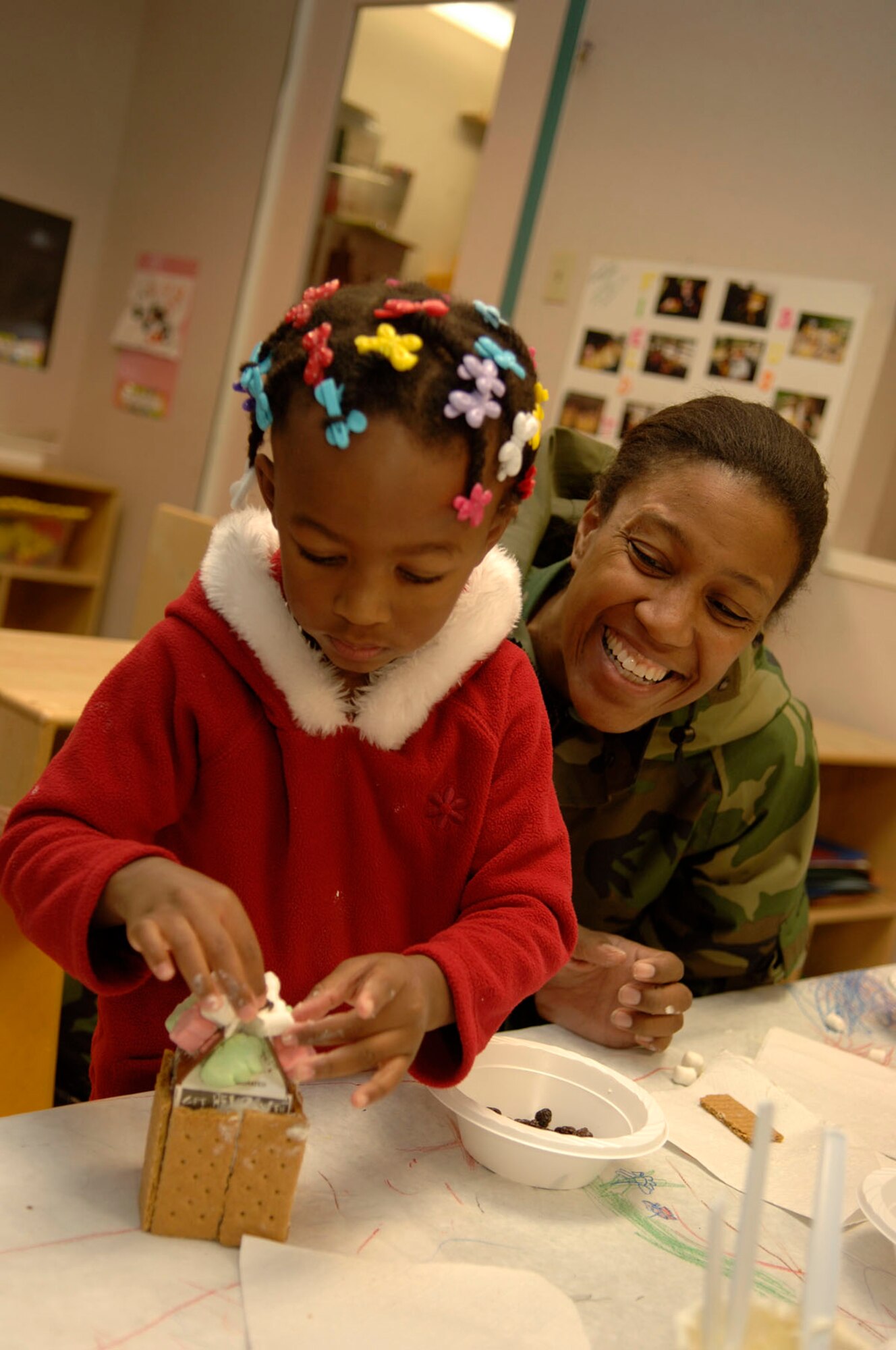 HANSCOM AFB, Mass. – The Child Development Center sponsored a parent and child activity on Dec. 7. Children in the pre-school program made gingerbread houses with their family members. Madison Whitehurst (left) adds the finishing touches to her gingerbread house while her mom, Maj. Pamela Howard looks on. (U.S. Air Force photo by Jan Abate)


