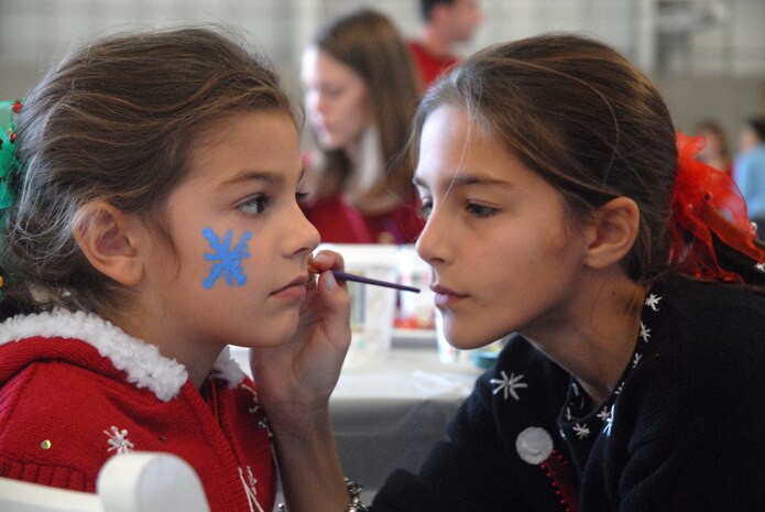 11, paints holiday objects on Sarah, her 6-year-old sister, during the Children's Holiday Party.  Both are daughters of Lt. Col. Johnny Lamontagne. (U.S. Air Force photo/Airman Melissa White)