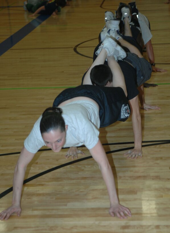 Senior Airman Jessica Aadalen leads the Civil Engineer Squadron's readiness warriors in a caterpillar push-up during the fitness survivor challenge, Dec. 07.  Teams have to do a push-up together while their legs are on the person behind them and last person is doing a regular push-up.  (U.S. Air Force photo / Airman 1st Class Joshua Seybert)