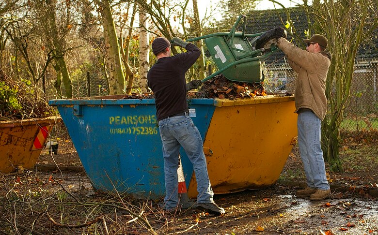Tech. Sgt. Brian Crandell, 95th Reconnaissance Squadron, pushes branches into a skip to pack them down during the squadron's community clean-up at Riverside Middle School in Mildenhall Dec. 7. Every year the 95th RS helps a school in the local community by cutting back and clearing overgrown areas. (U.S. Air Force photo by Karen Abeyasekere)