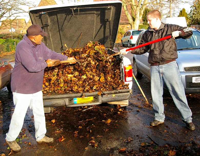 Master Sgt. Larry Haynes, left, and Senior Airman Sean Ellis, both 95th RS, transfer piles of leaves into the back of a truck, ready to transfer to the skip, Dec. 7 at a local school in Mildenhall. The squadron members spent two days cleaning up a large area of the school grounds. (U.S. Air Force photo by Karen Abeyasekere)