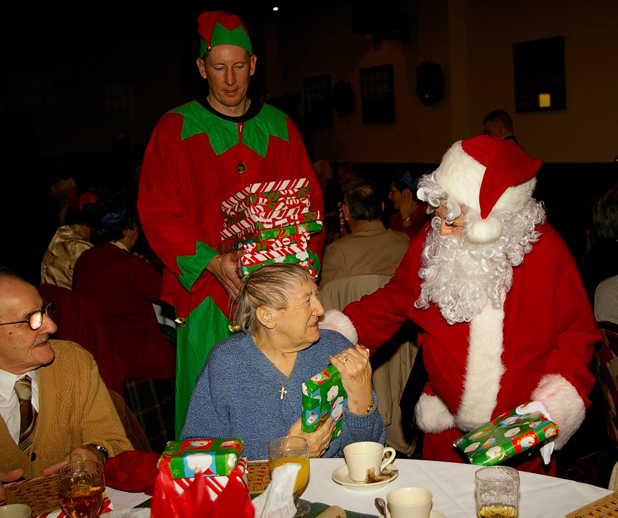 Violet Maley, from Mildenhall, gets her present from Santa, Dec. 5, as her husband, Fred, left, looks on. Mr. and Mrs. Maley were part of over 100 senior citizens who attended the Christmas luncheon at the Galaxy Club. (U.S. Air Force photo by Karen Abeyasekere)