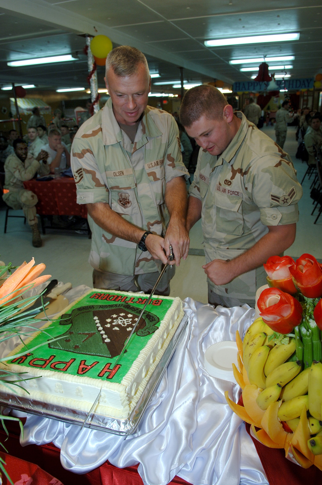 SOUTHWEST ASIA - Staff Sgt. Douglas Olsen, 379th Air Expeditionary Wing Public Affairs, and Airman 1st Class Nicholas Jansen, 379th Expeditionary Civil Engineer Squadron, cut the birthday cake as the oldest and youngest Airman celebrating a birthday in the month of December during a birthday dinner hosted by senior noncommissioned officers and officers at a Southwest Asia air base. Sergeant Olsen is deployed from Camp Murray, Wash. and Airman Jansen is deployed from Ramstein AB, Germany. (U.S.Air Force photo/Master Sgt. Greg Kunkle)