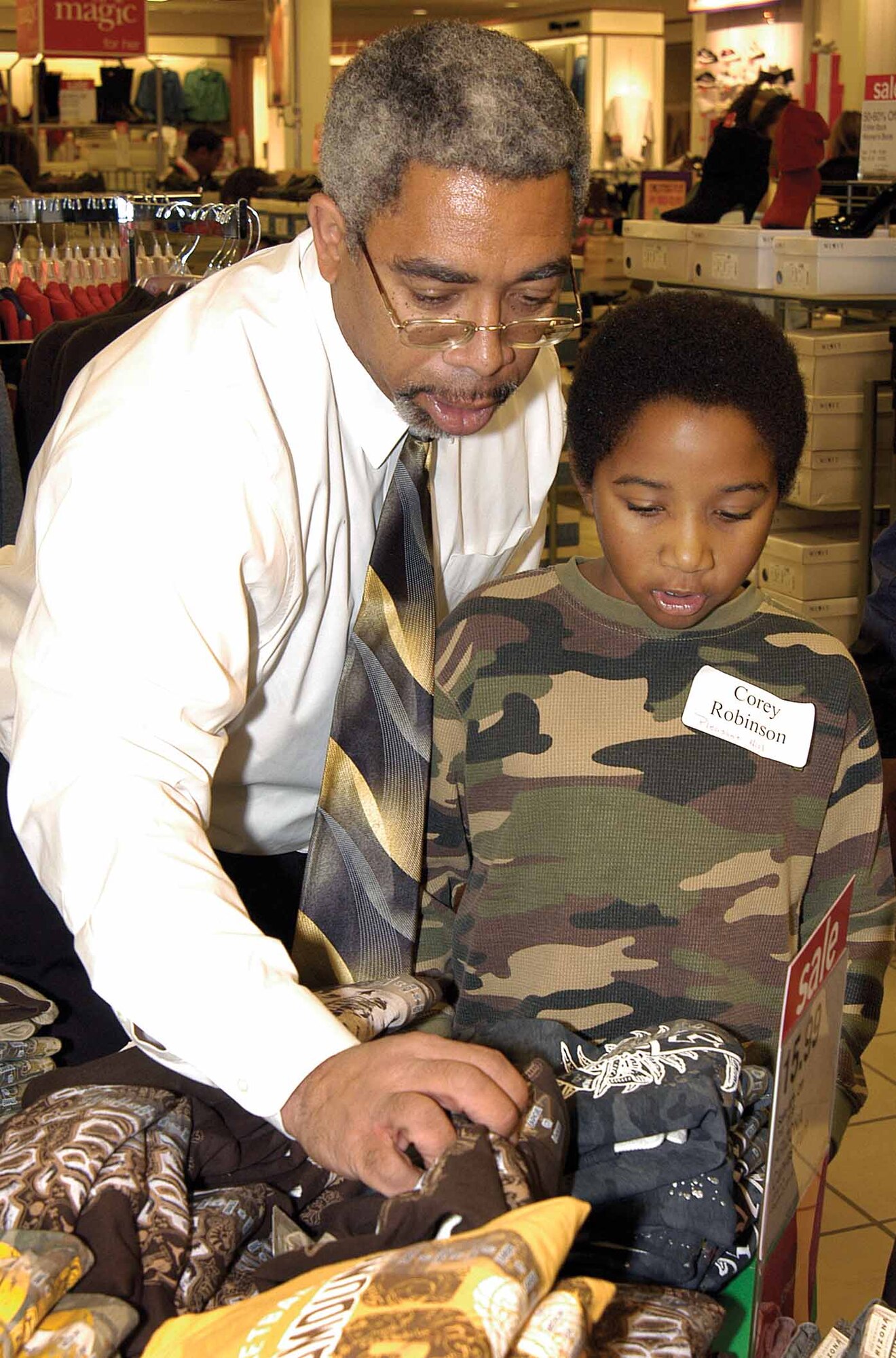 Gerald Joseph helps 8-year-old Corey Robinson find a new shirt during a Dec. 5 shopping fest at JC Penney.  The 727th Aircraft Sustainment Group employee is a veteran volunteer for the annual holiday event that provides new clothes for Mid-Del school children.  (Air Force photo by Margo Wright)
