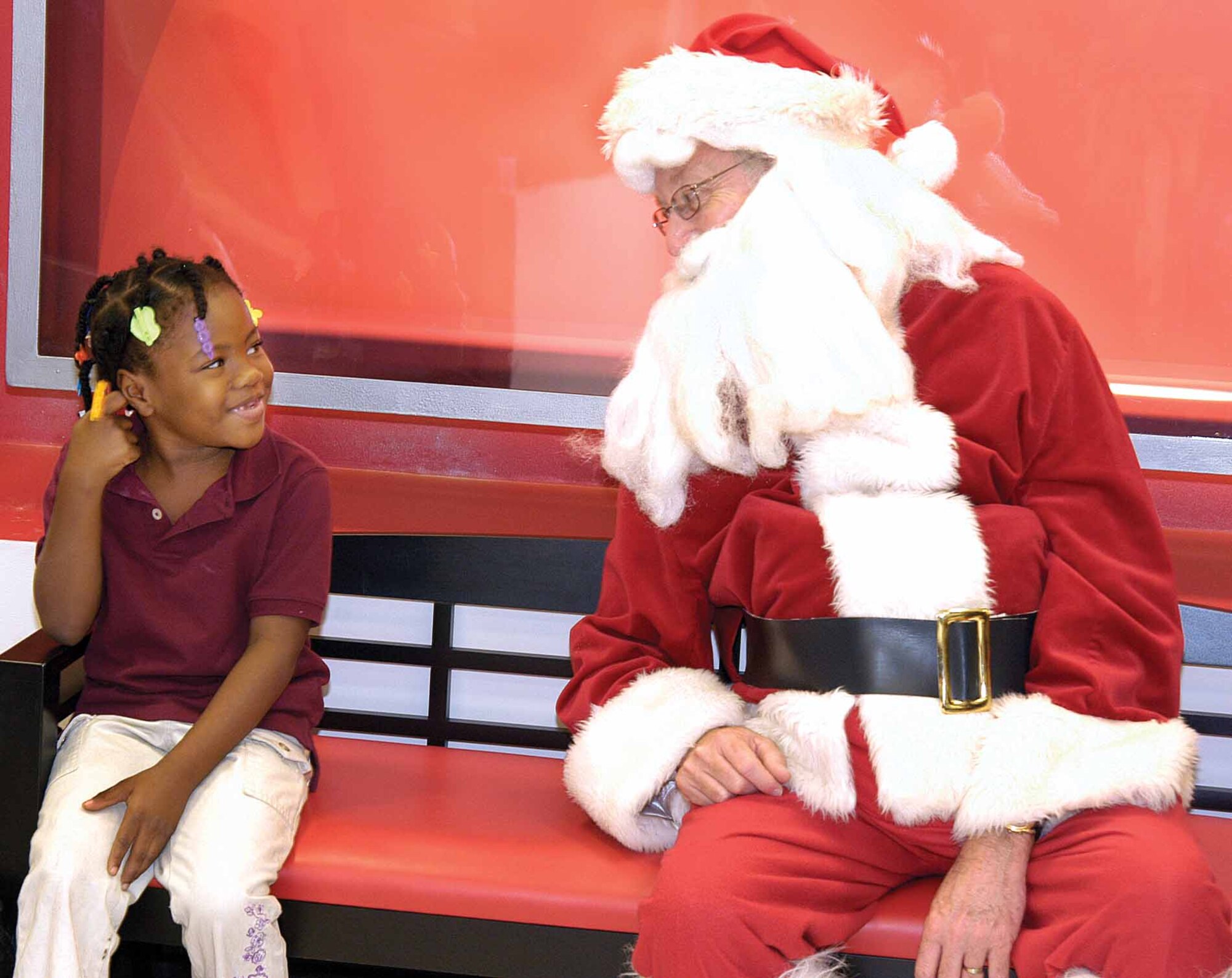 Mid-Del kindergartener Kyshaunna Broades shares a bench with Santa after shopping for new clothes with a B-52 Program Office volunteer during the annual Clothe-A-Kid event at JC Penney.  As Santa, Andy Jackson posed for photos with the children Dec. 6 and gave out candy canes and new backpacks filled with goodies. (Air Force photos by Margo Wright)