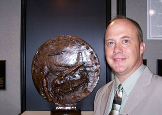 Chief Master Sgt. Rodney Christa stands with the bronze plaque that will be placed at Mobility Memorial Park at Scott AFB. The bust has a C-130 being loaded by aeromedical troops while a C-17 comes into to land. The Bronze work is in honor of the Airlift Tanker Association Hall of Fame's Aeromedical Evacuation Team. Chief Christa was inducted into the ATA AE Legacy Team in honor of his service during OIF and his leadership in evacuating medical patients from New Orleans after Hurricane Katrina ravaged the Gulf Coast Area. Chief Christa's direction and innovation during the emergency helped pave the way for new national disaster response plans to be implemented in the event of a catastrophic disaster or terrorist attack. (Courtesy Photo)