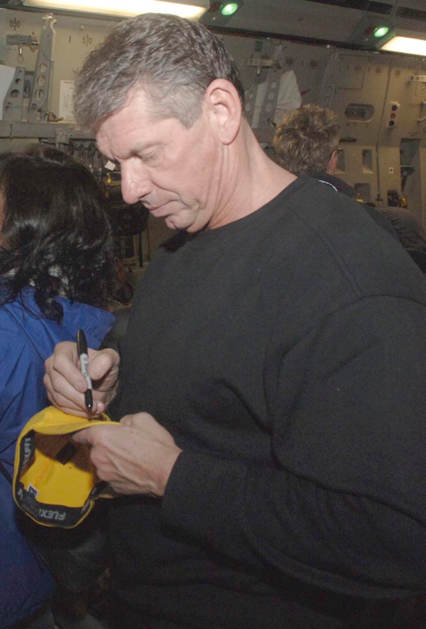 Vincent McMahon Jr., Chairman, World Wrestling Entertainment, autographs a hat for family members of returning Airmen and Soldiers from Iraq aboard a C-17 here, Dec. 8.