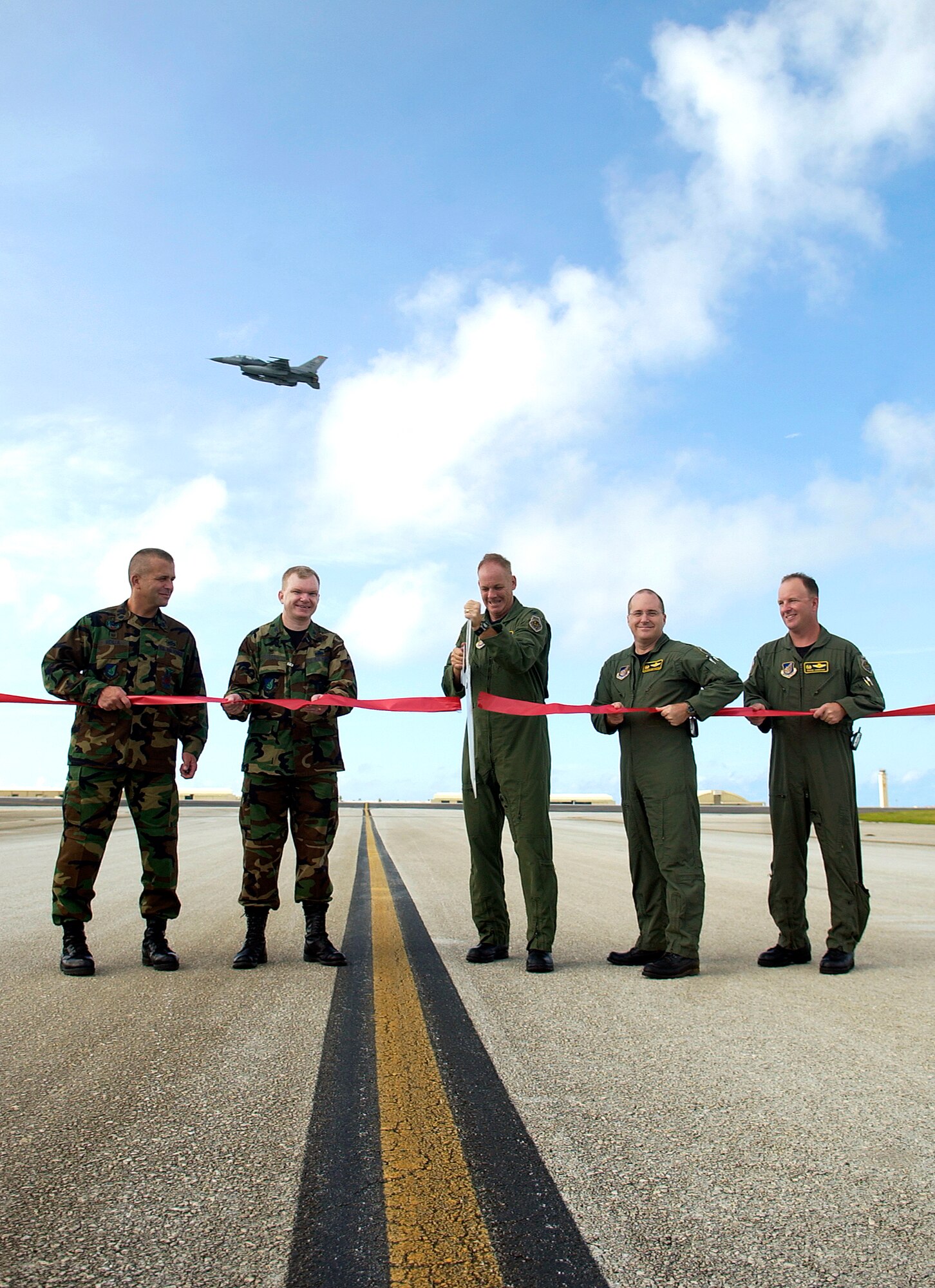 As Brig. Gen. Douglas Owens, 36th Wing commander, flies over in an F-16 Fighting Falcon, Lt. Col. Peter Ridilla, 36th Civil Engineering Squadron commander; Col. Mark Talley, 36th Mission Group commander; Col. Joel Westa, former 36th Wing vice commander; Col. Damien McCarthy, 36th Operations Group commander; and Lt. Col. Dave Hornyak, 36th Operations Support Squadron commander cut the ribbon marking the official opening of the new runway June 18. (U.S. Air Force photo/Senior Airman Miranda Moorer)                              