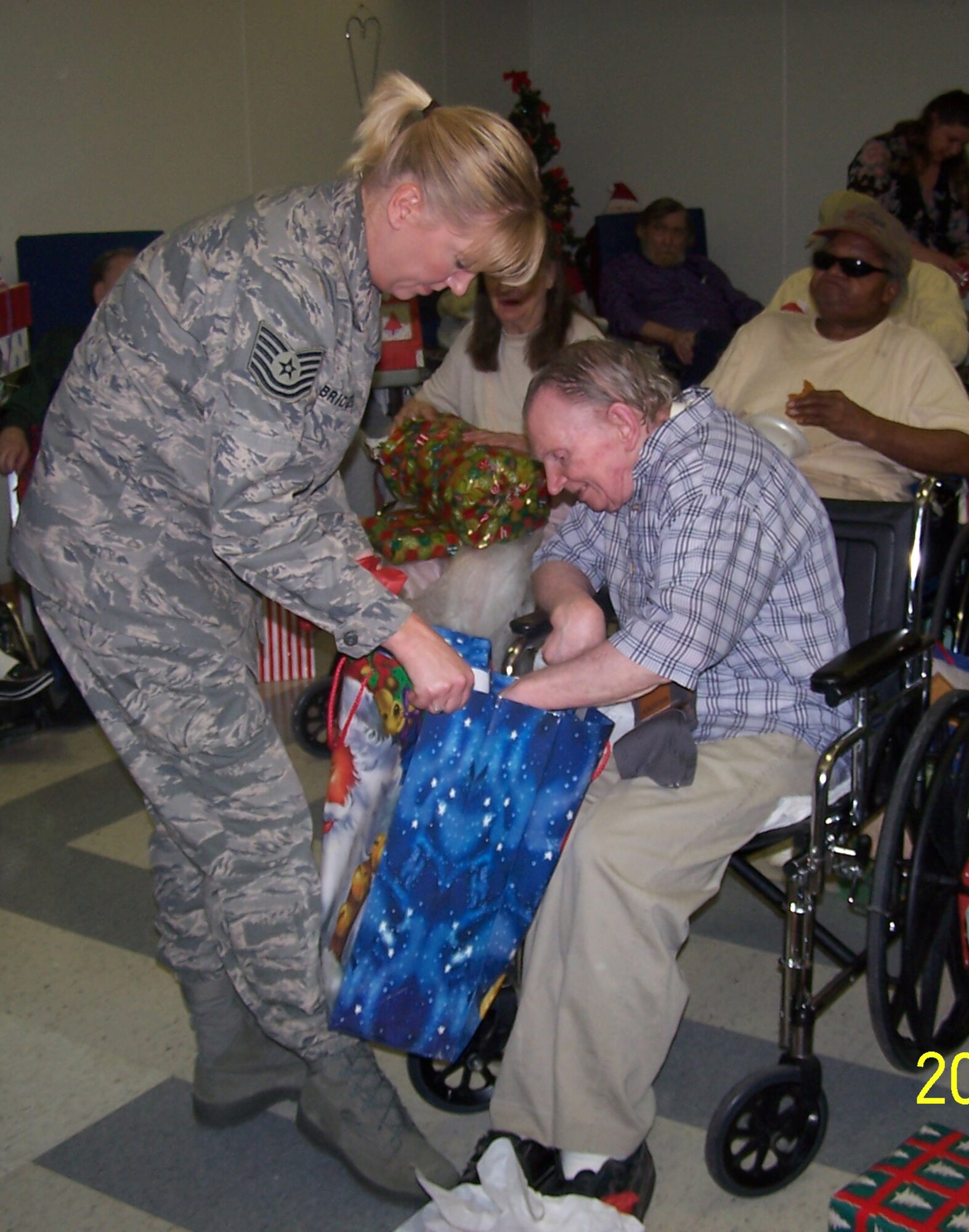 WARRENSBURG, Mo. -- Tech. Sgt. Alison Bridges, 509th Communications Squadron, helps a Johnson County Care Center resident open a gift Dec. 13. More than 25 members of the 509th CS sang carols, passed out drinks and cookies and distributed presents that members of the squadron had bought for the residents. (Photo printed with permission of Chief Master Sgt. John Blair) 