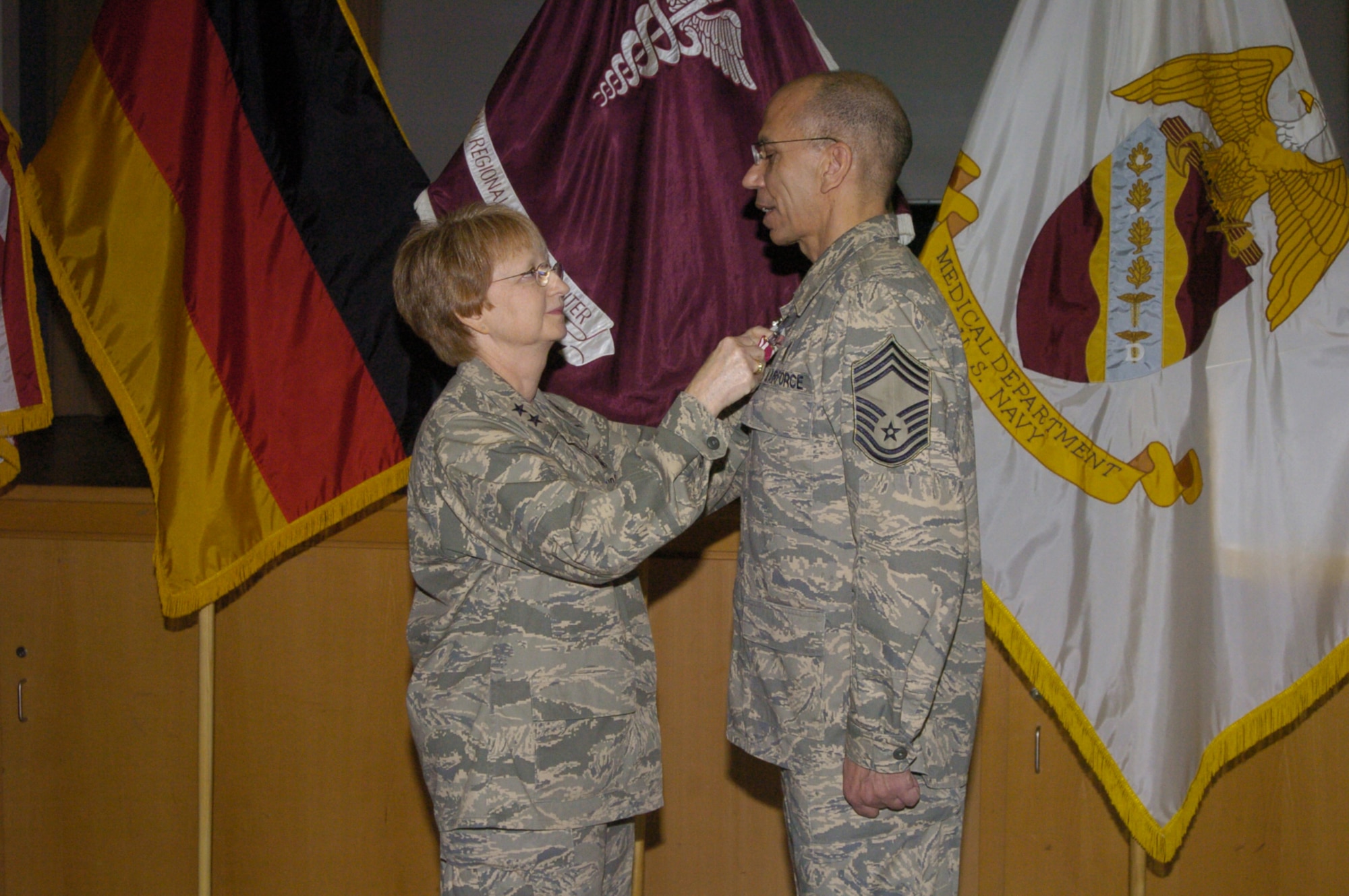 Major Gen. Melissa Rank, the Assistant Air Force Surgeon General for Nursing Services and Medical Force Development, presents Chief Master Sgt. David Lewis, the enlisted advisor to the Assistant Air Force Surgeon General for Nursing Services, with the Meritorious Service Medal during a  Dec. 12 ceremony at Landstuhl Regional Medical Center. The official ceremony was followed by an emotional coin presentation by Rank to Lewis' father. (U.S. Army Photo/Chuck Roberts)